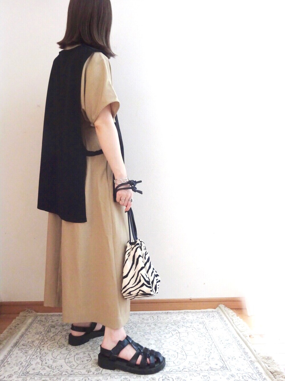 ブラック系のベスト、ベージュ系のワンピース、その他のショルダーバッグを着用したレディースの夏コーディネートの2枚目の写真
