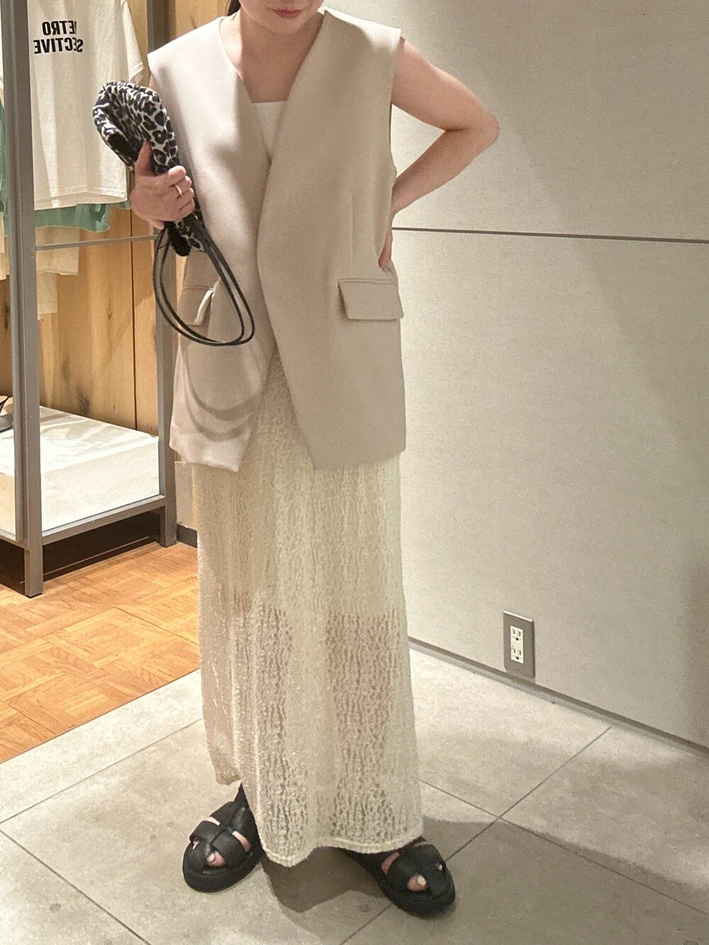 ベージュ系のベスト、ホワイト系のスカート、ブラック系のサンダルを着用したレディースの春コーディネートの3枚目の写真