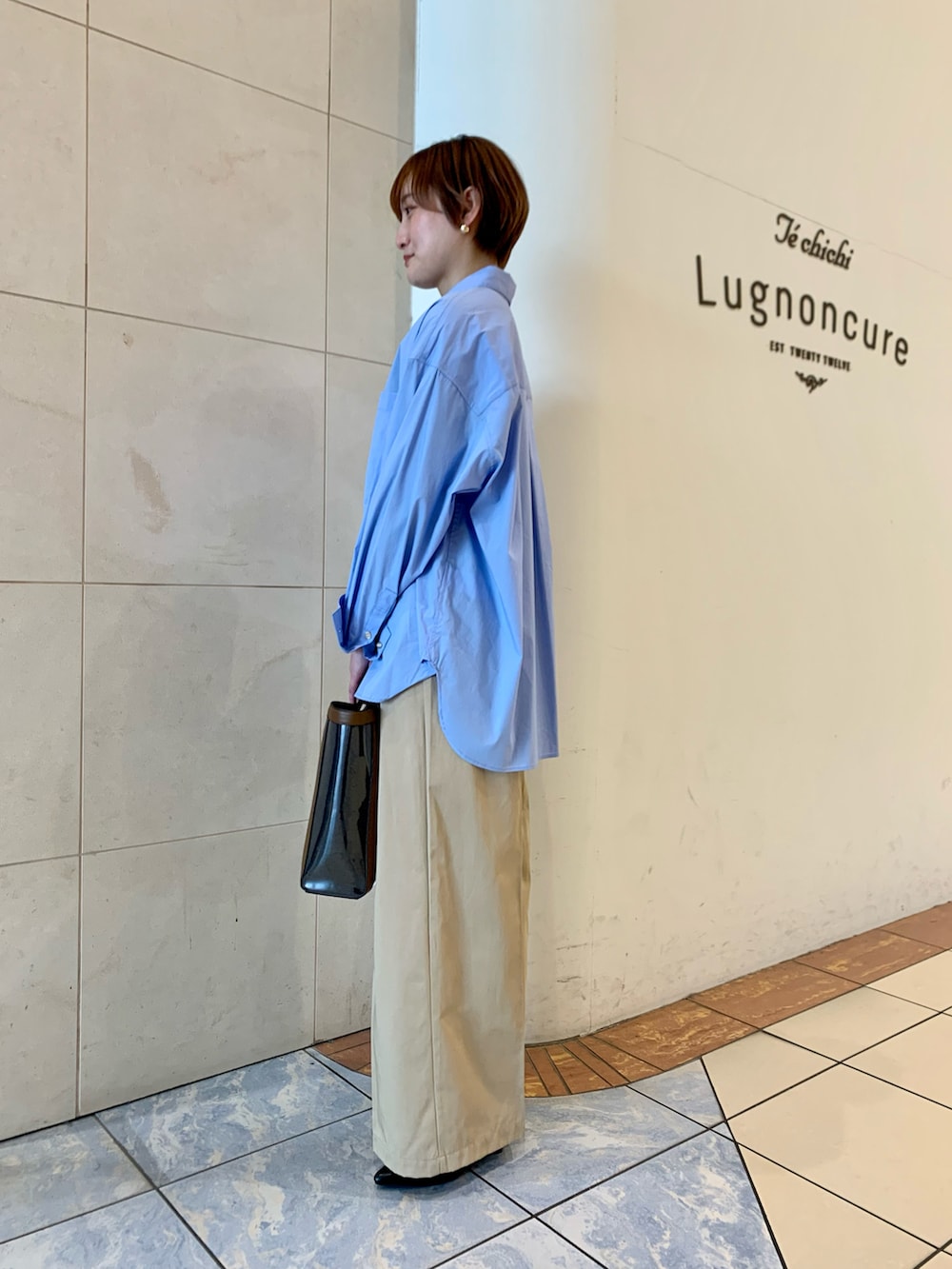 ブルー系のシャツ/ブラウス、ベージュ系のチノパンツ、ブルー系のハンドバッグを着用したレディースの春コーディネートの2枚目の写真