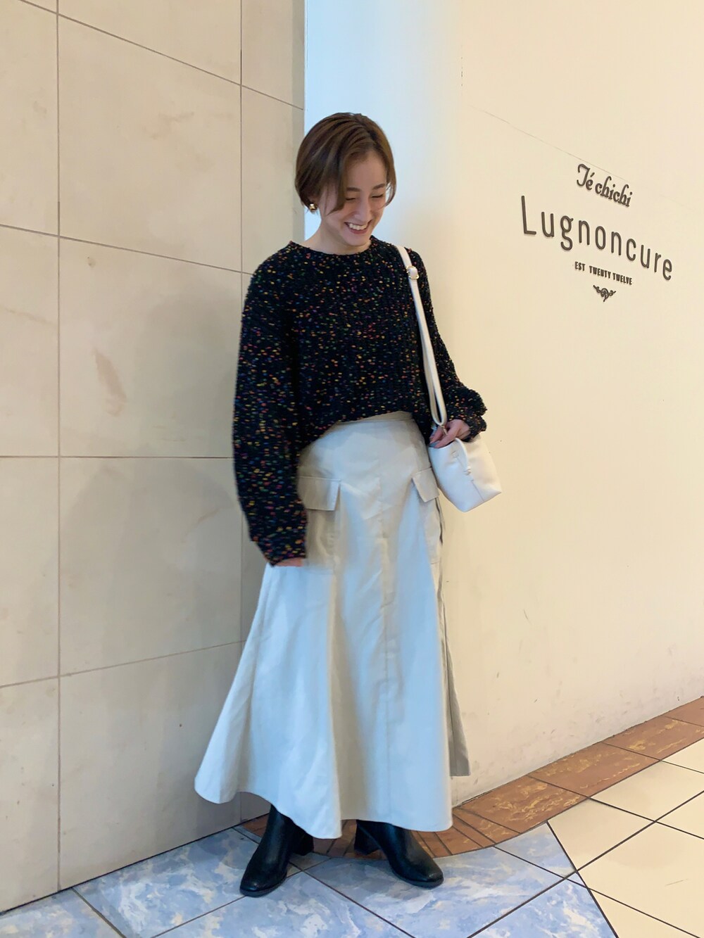 ブラック系のニット/セーター、ホワイト系のスカート、ブラック系のブーツを着用したレディースの冬コーディネートの2枚目の写真