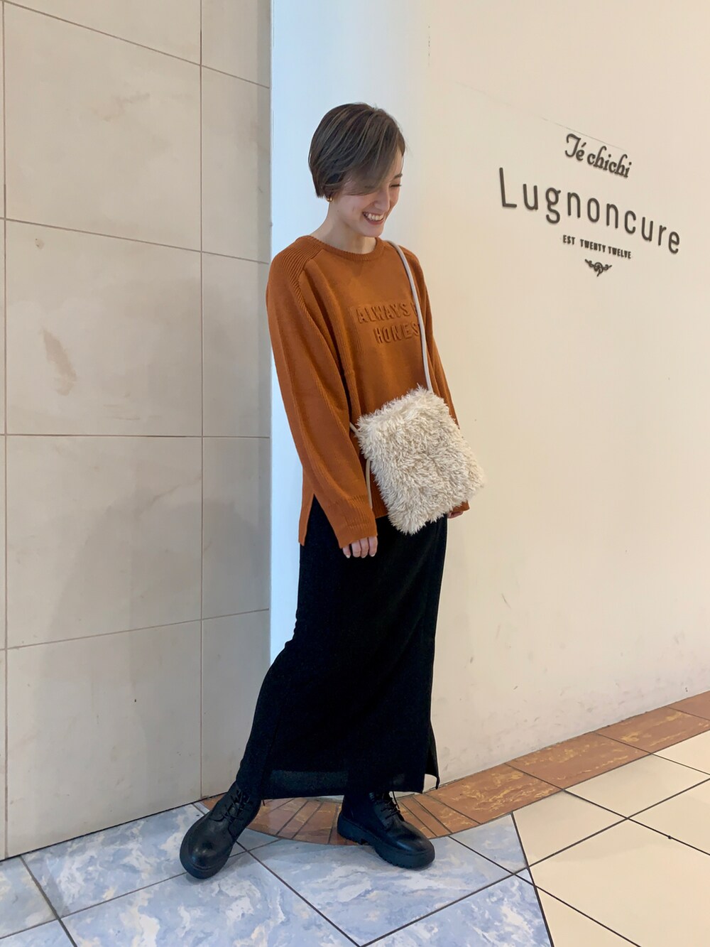 ブラック系のスカート、ブラック系のブーツ、ホワイト系のハンドバッグを着用したレディースの秋コーディネートの2枚目の写真