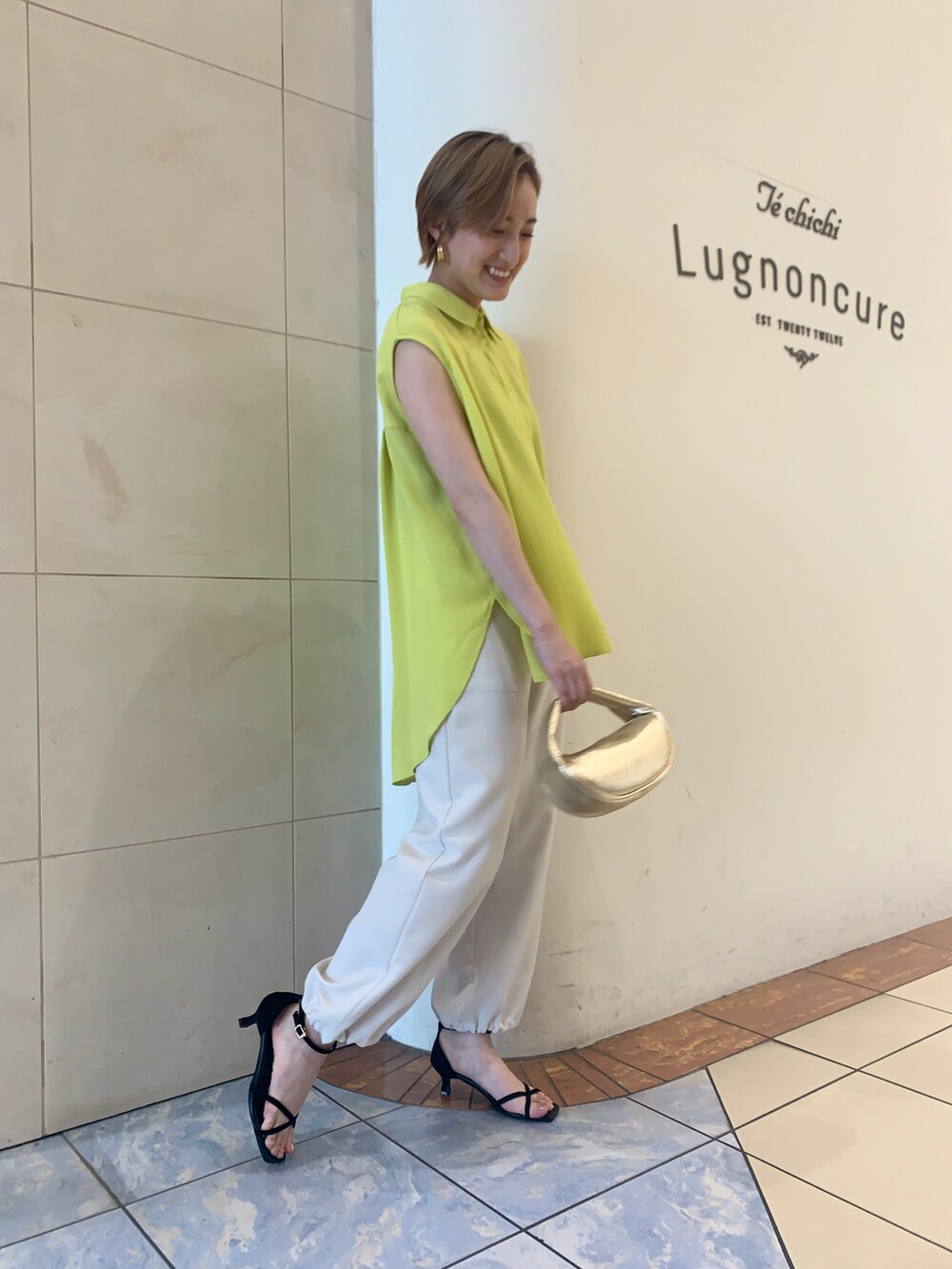 ホワイト系のカーゴパンツ、ブラック系のサンダル、ゴールド系のハンドバッグを着用したレディースの夏コーディネートの2枚目の写真