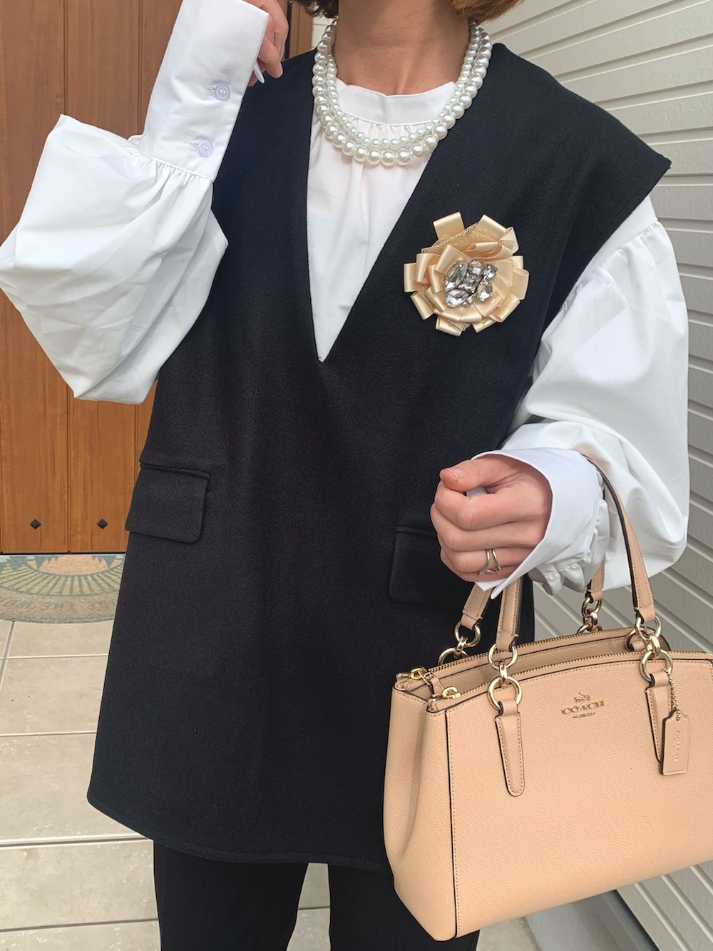 ブラック系のベスト、ホワイト系のシャツ/ブラウス、ベージュ系のハンドバッグを着用したレディースの冬コーディネートの3枚目の写真