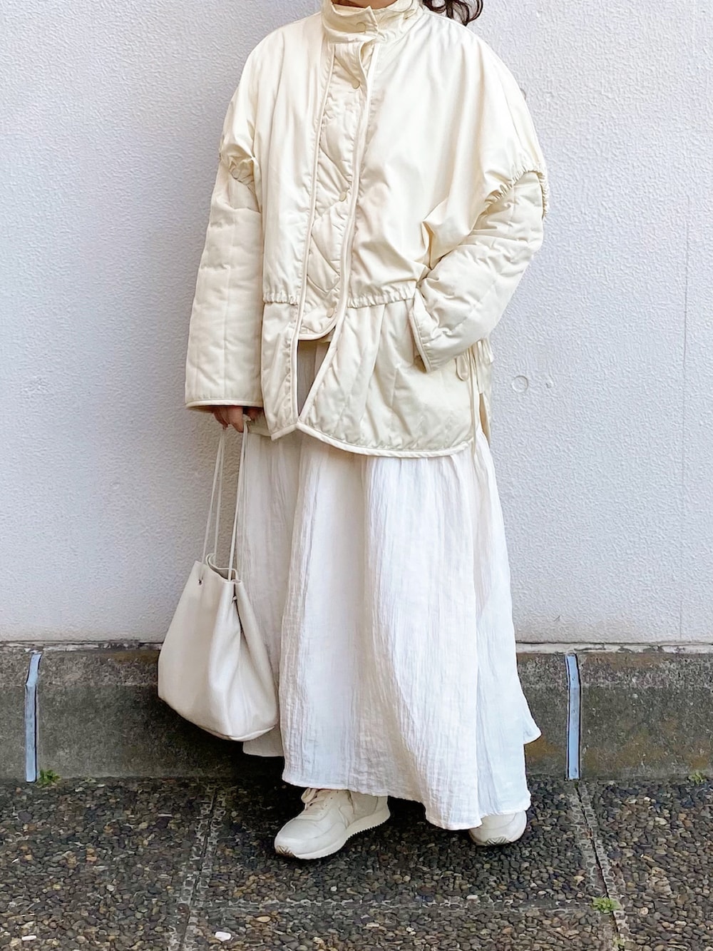 オレンジ系のニット/セーター、ホワイト系のスカート、ホワイト系のハンドバッグを着用したレディースの冬コーディネートの2枚目の写真