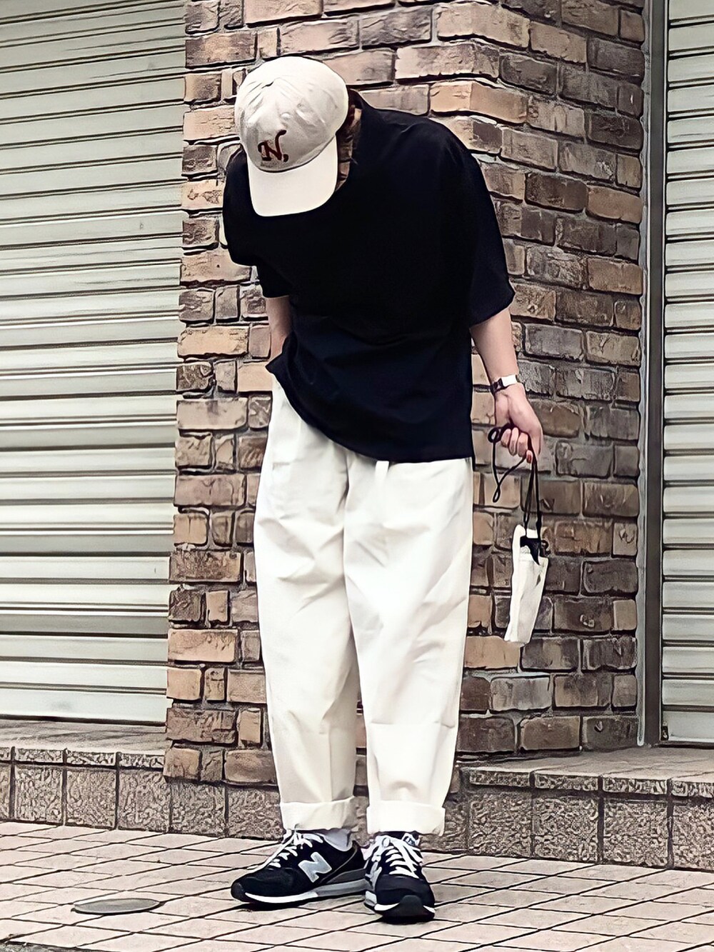 ブラック系のポロシャツ、ホワイト系のチノパンツ、ホワイト系のバッグを着用したメンズの夏コーディネートの2枚目の写真