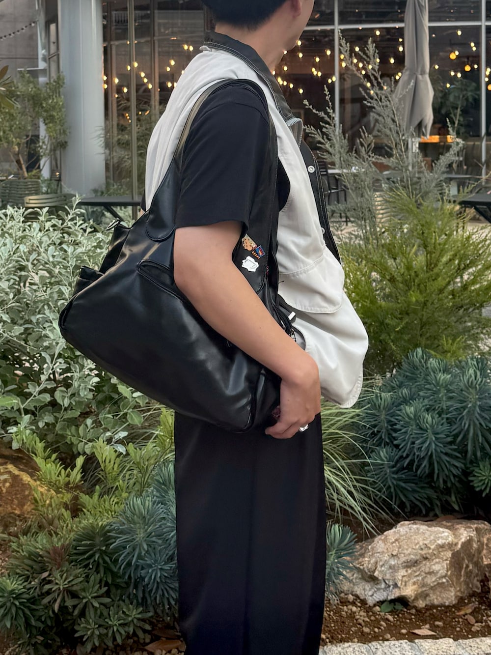 ブラック系のスラックス、ホワイト系のベスト、ブラック系のショルダーバッグを着用したメンズの秋コーディネートの2枚目の写真