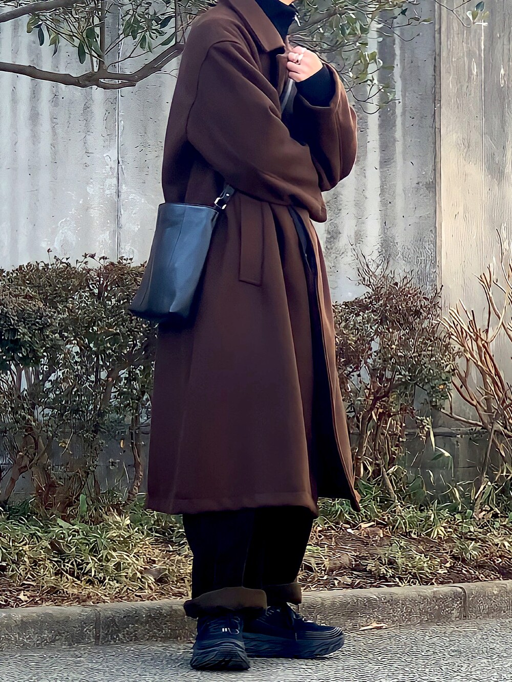 ブラウン系のステンカラーコート、ブラック系のショルダーバッグ、ブラウン系のその他パンツを着用したメンズの冬コーディネートの2枚目の写真