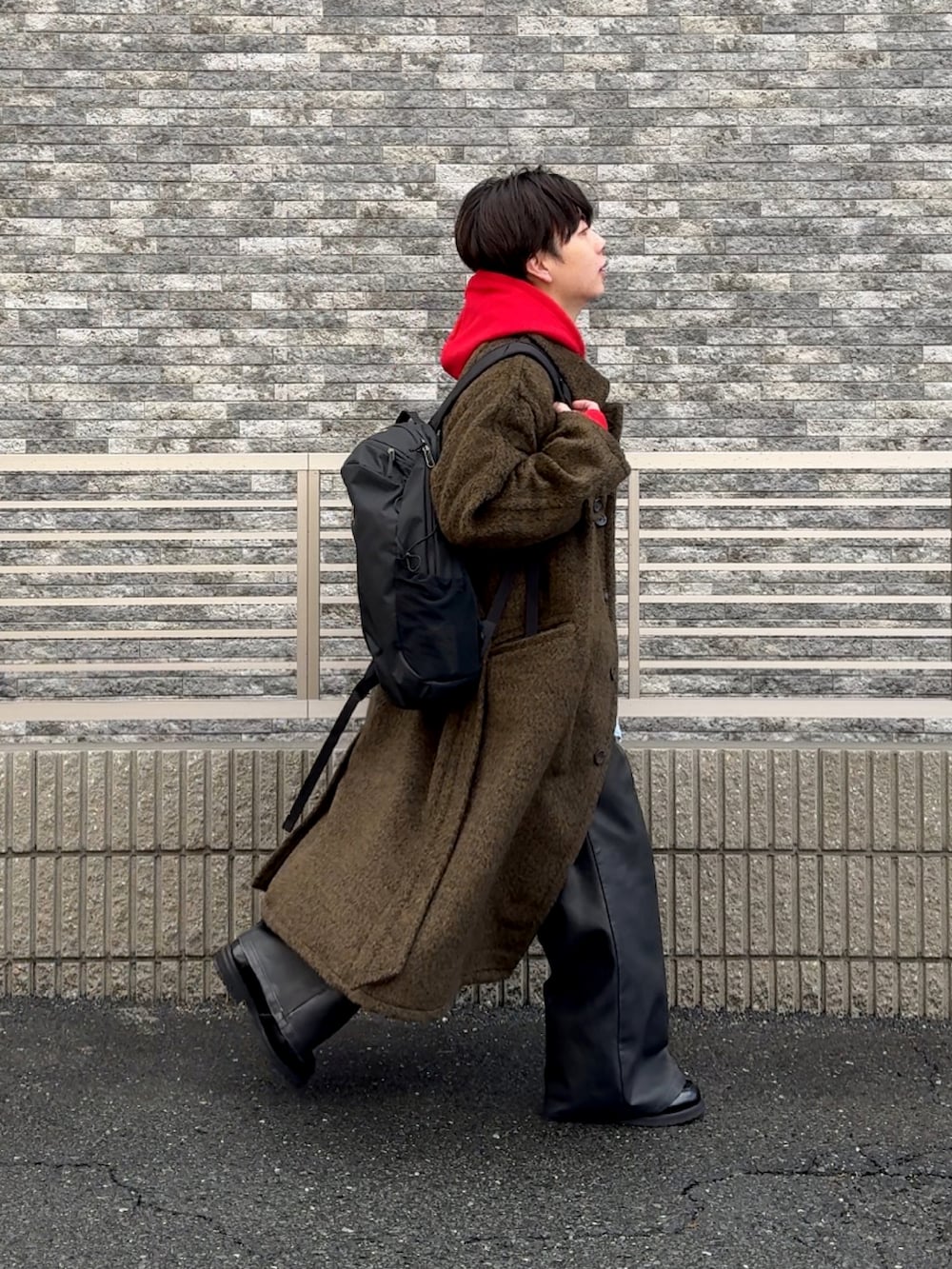 ブラック系のその他パンツ、ブラウン系のステンカラーコート、レッド系のパーカーを着用したメンズの冬コーディネートの2枚目の写真