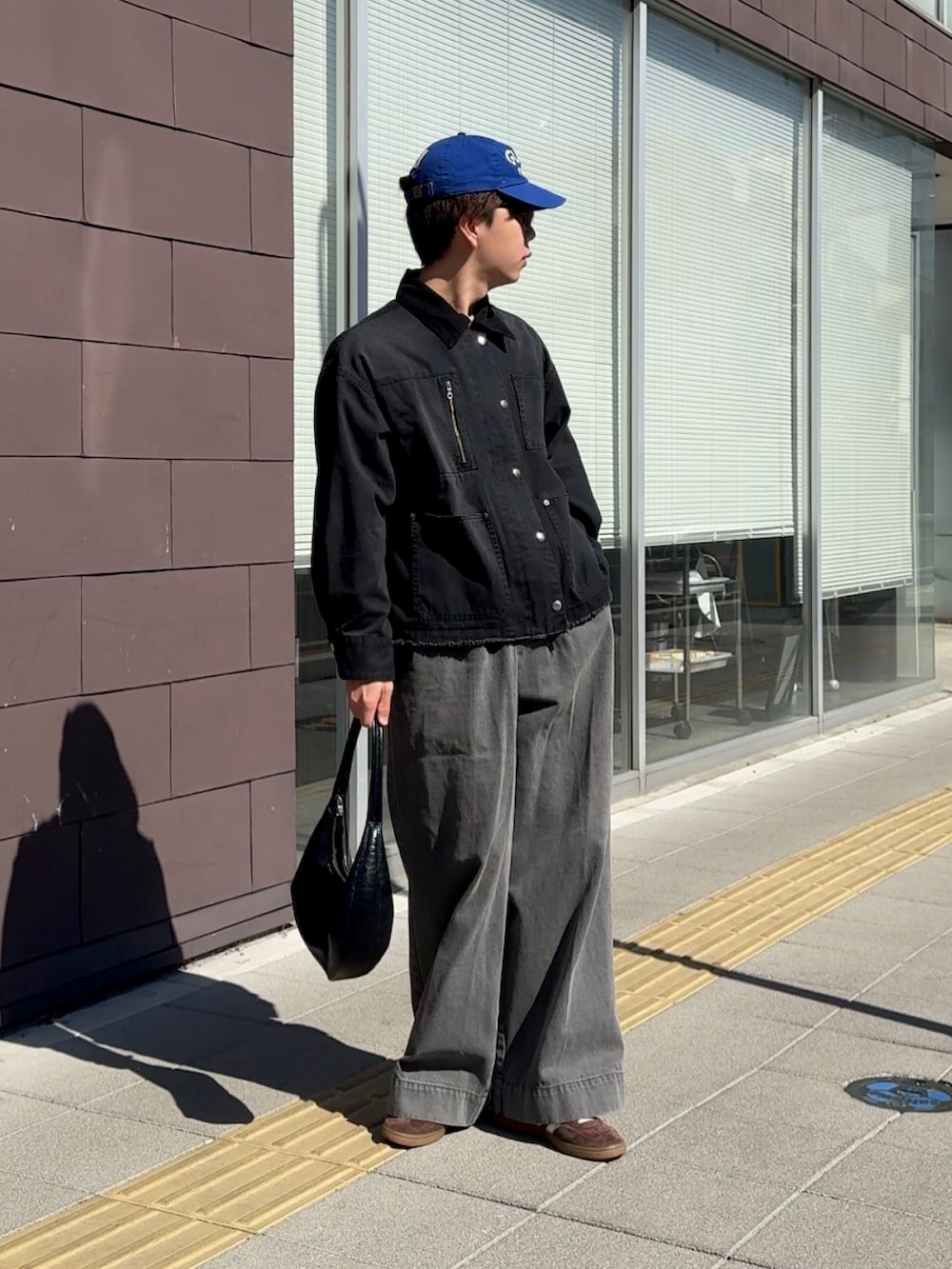 ブラック系のデニムジャケット、ブラック系のハンドバッグ、グレー系のデニムパンツを着用したメンズの春コーディネートの2枚目の写真