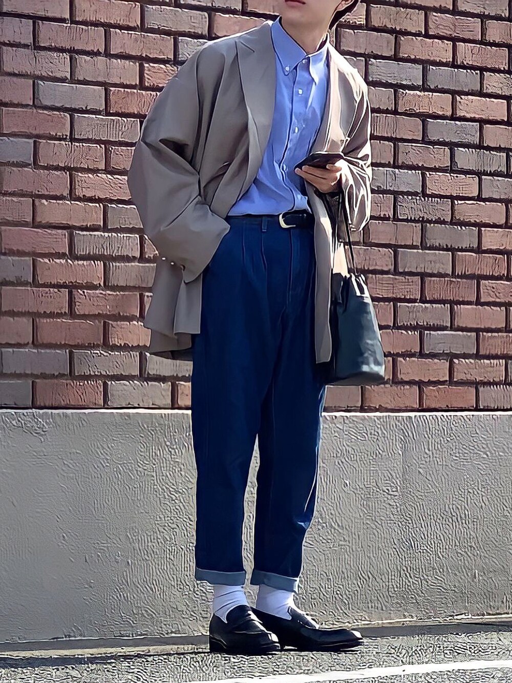 ブラック系のハンドバッグ、ブルー系のデニムパンツ、ブラック系のローファーを着用したメンズの秋コーディネートの3枚目の写真