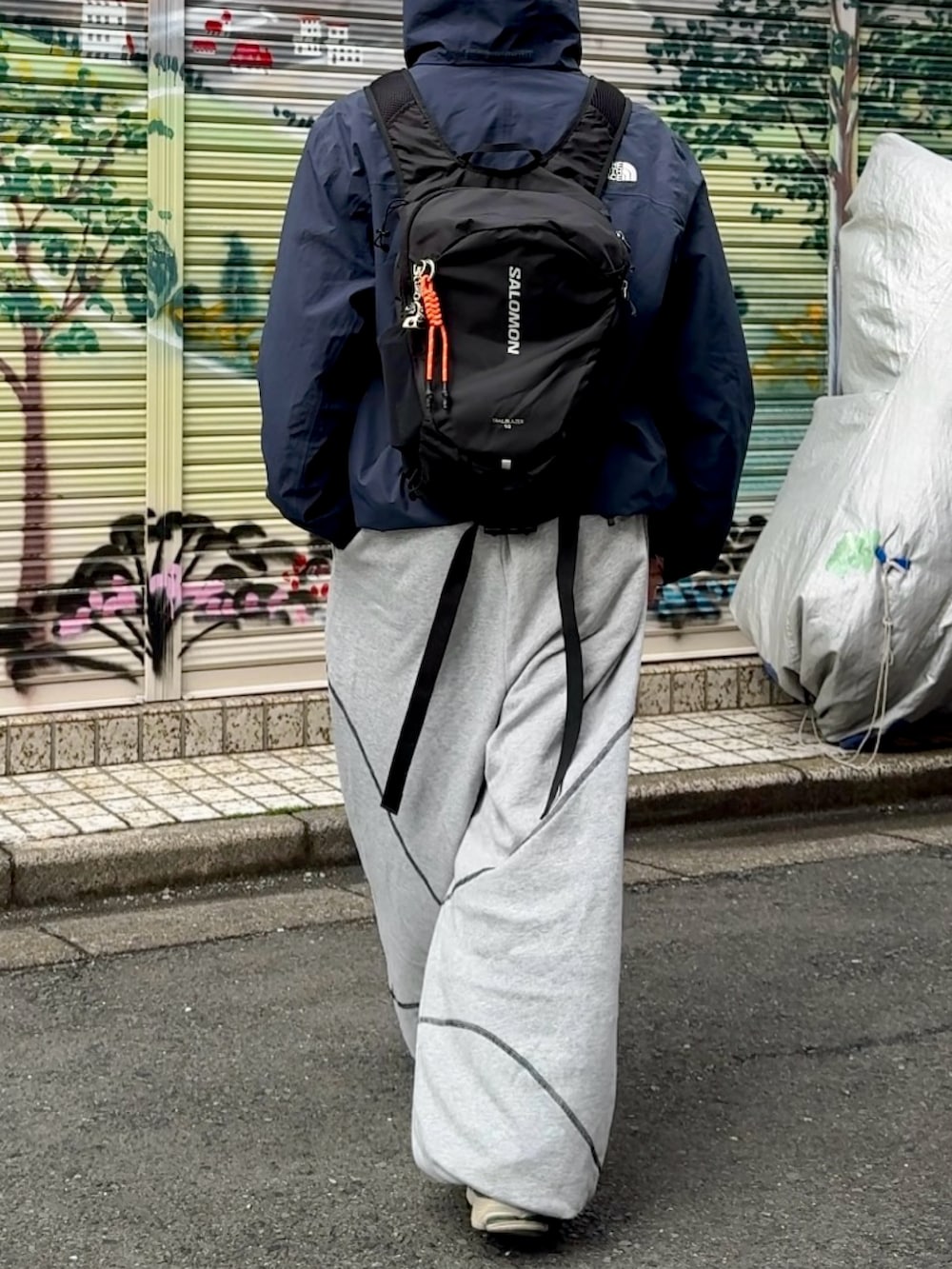 グレー系のスウェットパンツ、ブラック系のナイロンジャケット、ブラック系のバックパック/リュックを着用したメンズの春コーディネートの2枚目の写真