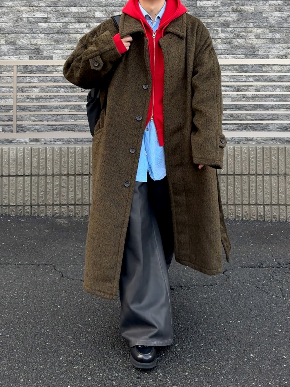 ブラック系のその他パンツ、ブラウン系のステンカラーコート、レッド系のパーカーを着用したメンズの冬コーディネートの4枚目の写真