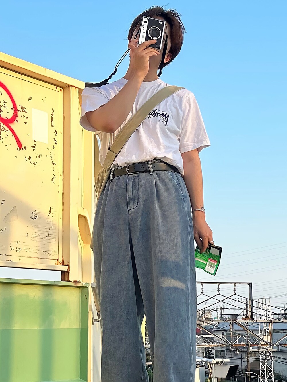 ブルー系のデニムパンツ、ホワイト系のTシャツ/カットソー、ベージュ系のメッセンジャーバッグを着用したメンズの夏コーディネートの4枚目の写真