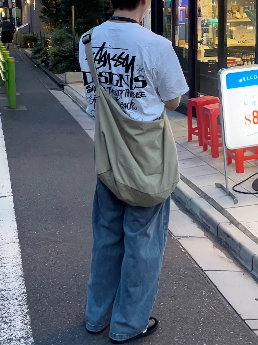 ブルー系のデニムパンツ、ホワイト系のTシャツ/カットソー、ベージュ系のメッセンジャーバッグを着用したメンズの夏コーディネートの2枚目の写真