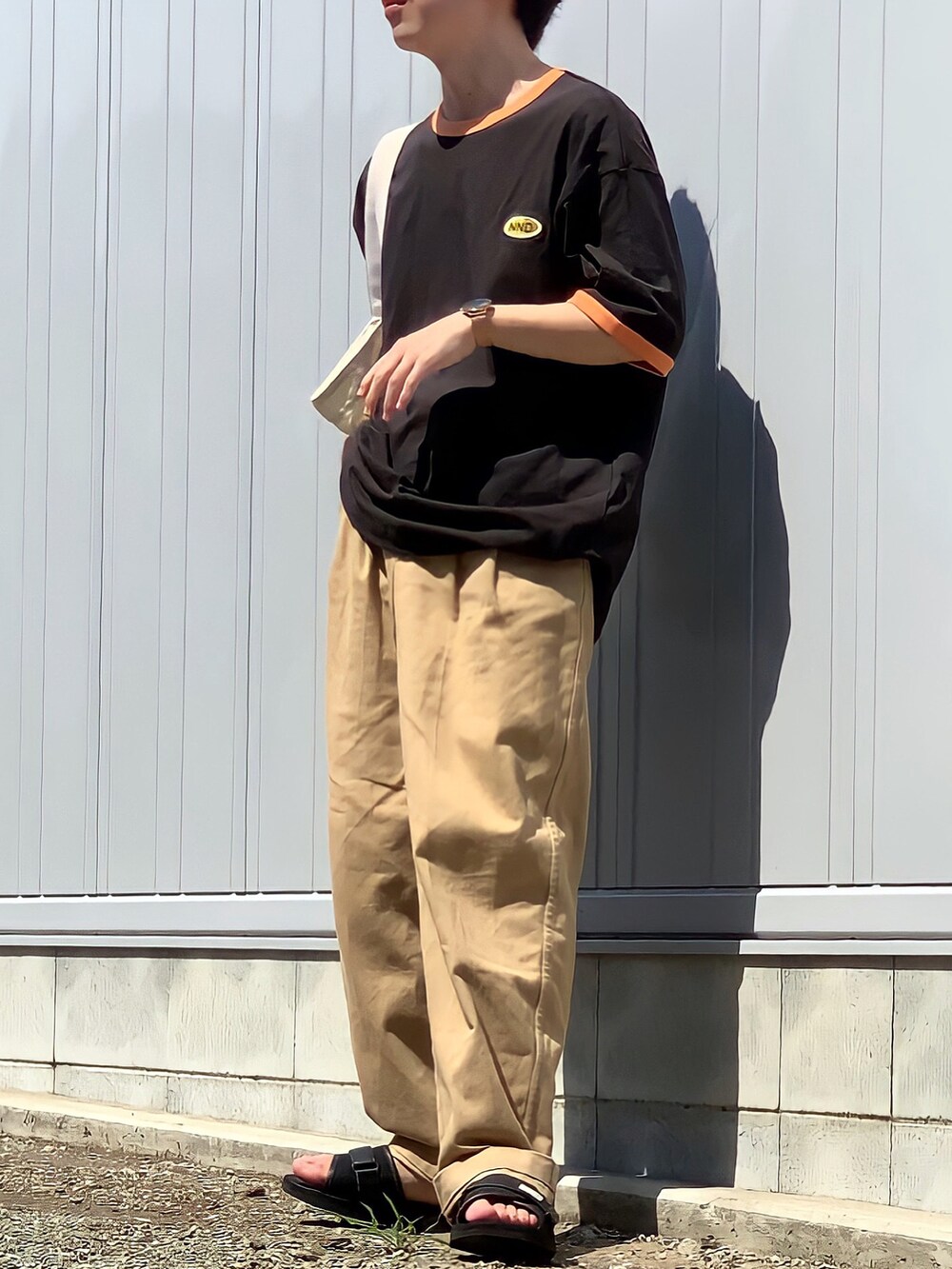 ベージュ系のチノパンツ、ブラウン系のTシャツ/カットソー、ホワイト系のトートバッグを着用したメンズの夏コーディネートの2枚目の写真