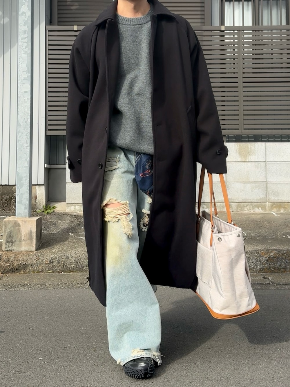 ブラック系のステンカラーコート、グレー系のニット/セーター、ブルー系のデニムパンツを着用したメンズの冬コーディネートの2枚目の写真