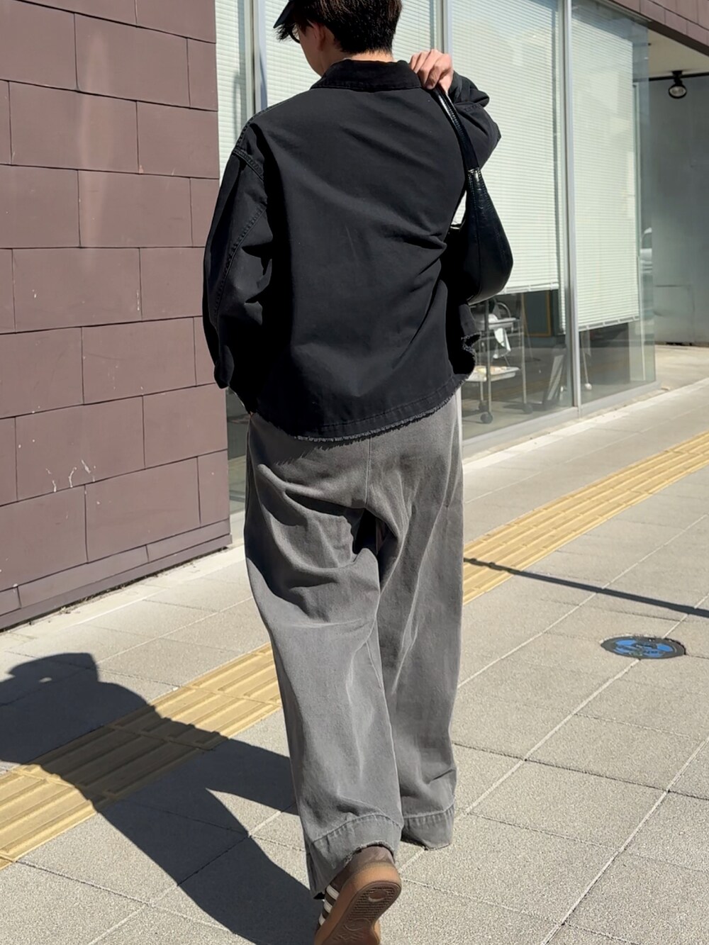 ブラック系のデニムジャケット、ブラック系のハンドバッグ、グレー系のデニムパンツを着用したメンズの春コーディネートの3枚目の写真