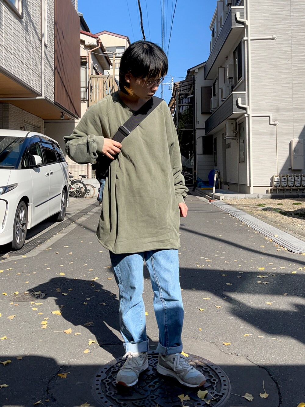 ブルー系のデニムパンツ、グリーン系のトップス、ブラック系のショルダーバッグを着用したレディースの秋コーディネートの2枚目の写真