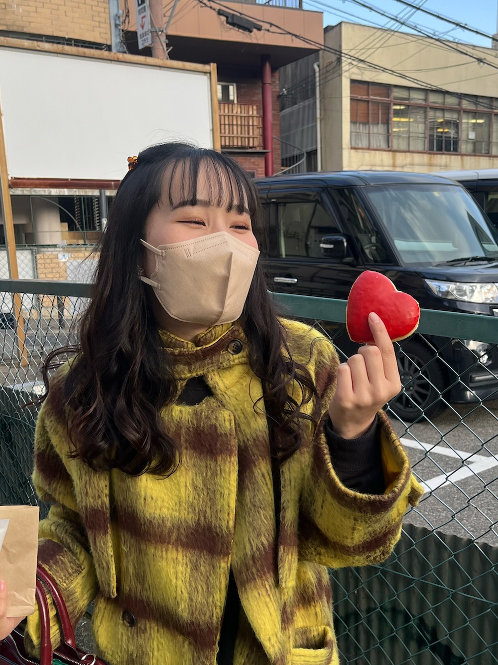 イエロー系のチェスターコート、レッド系のハンドバッグ、ブラック系のブーツを着用したレディースの冬コーディネートの2枚目の写真