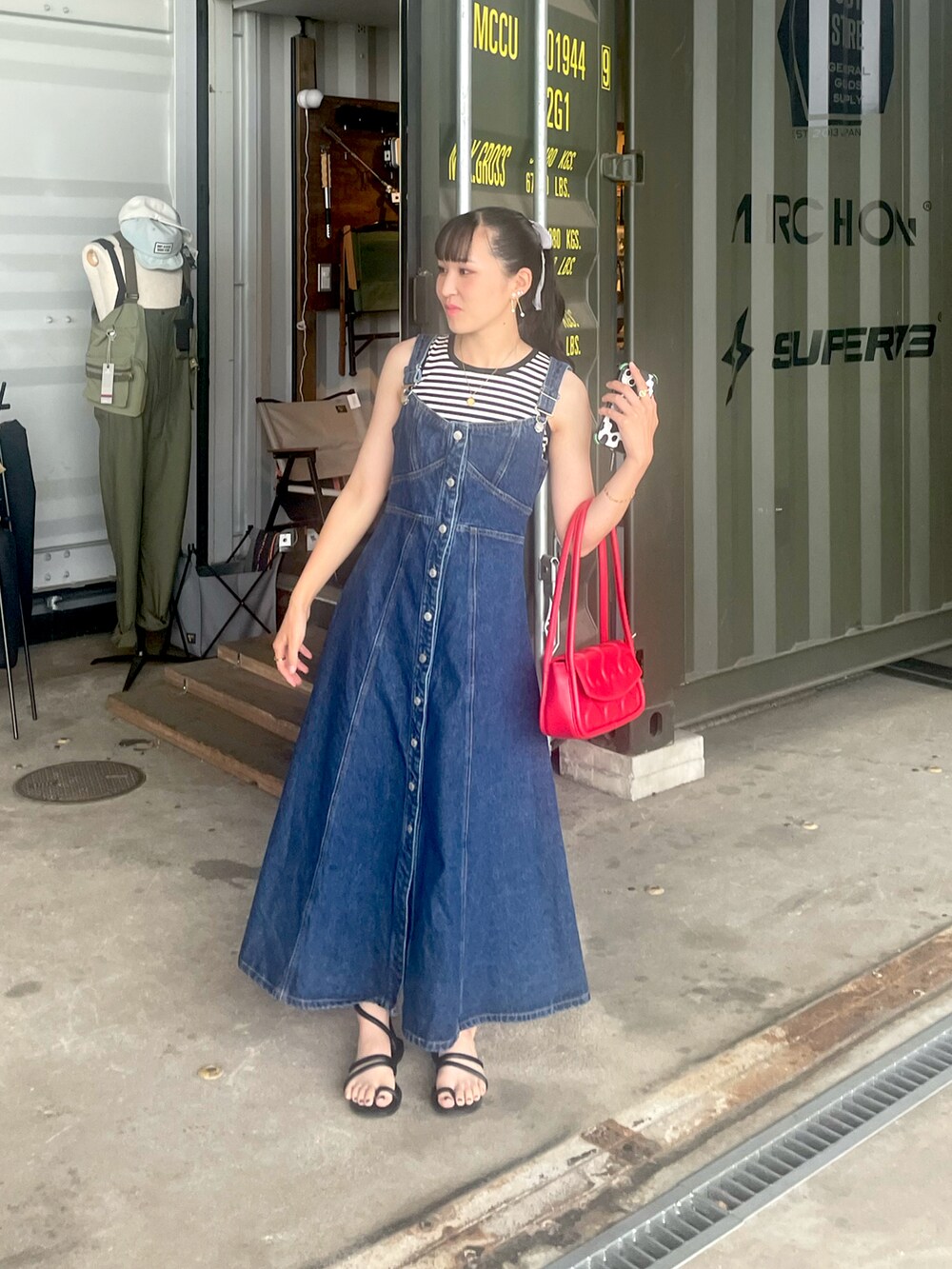 ブラック系のトップス、レッド系のバッグ、ブルー系のジャンパースカートを着用したレディースの夏コーディネートの2枚目の写真