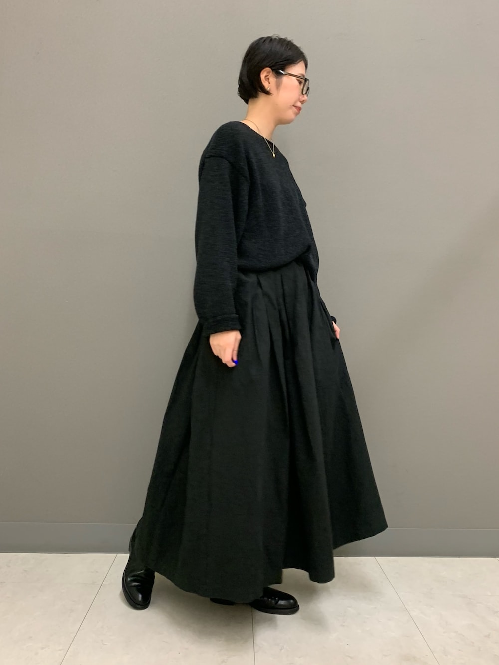 ブラック系のスカート、ブラック系のニット/セーター、ブラック系のブーツを着用したレディースの秋コーディネートの2枚目の写真