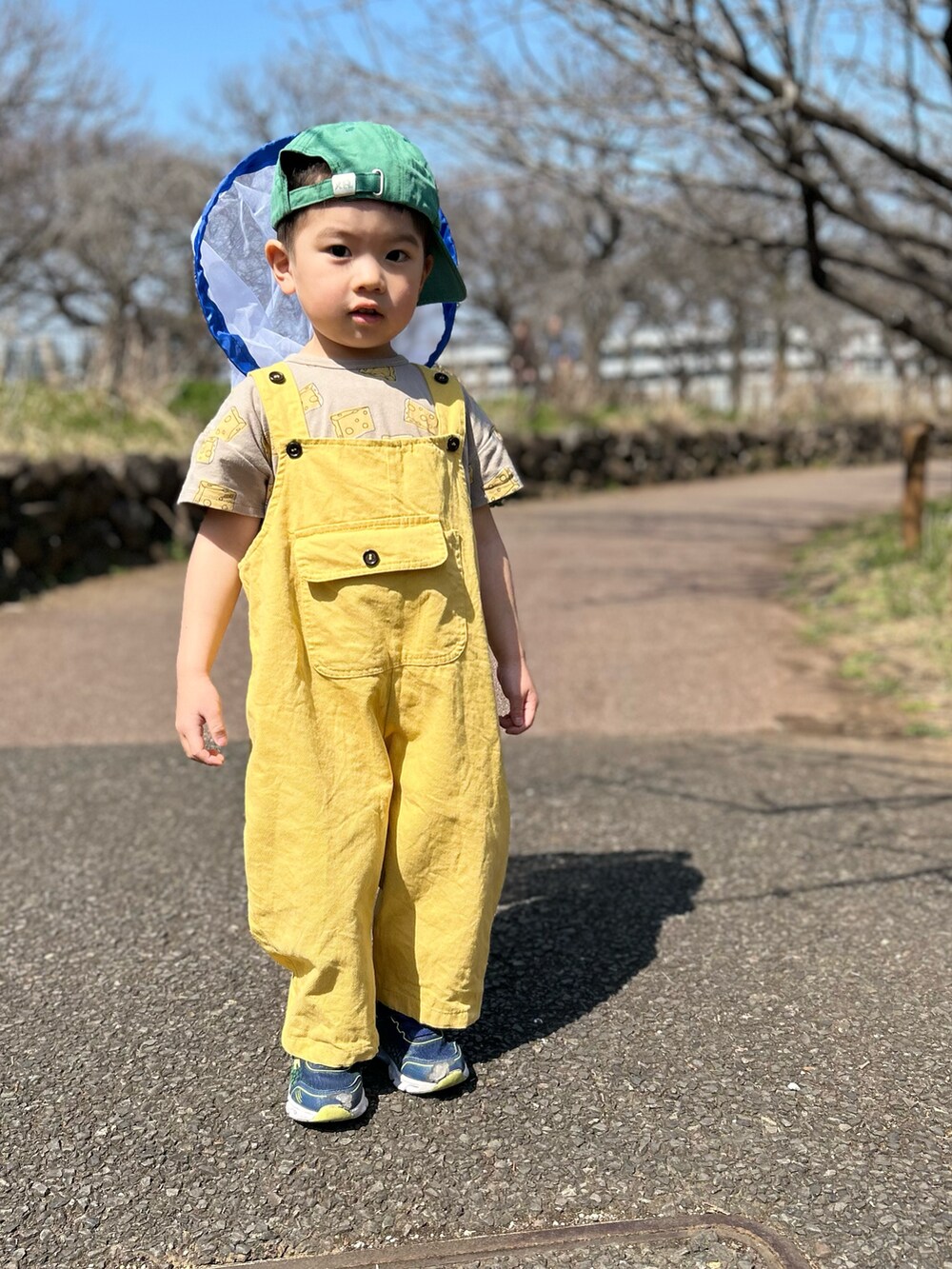 イエロー系のサロペット/オーバーオール、ベージュ系のTシャツ/カットソー、グリーン系のキャップを着用したキッズの夏コーディネートの3枚目の写真