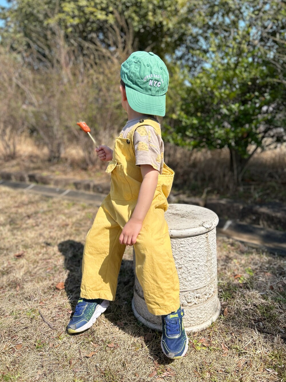 イエロー系のサロペット/オーバーオール、ベージュ系のTシャツ/カットソー、グリーン系のキャップを着用したキッズの夏コーディネートの2枚目の写真