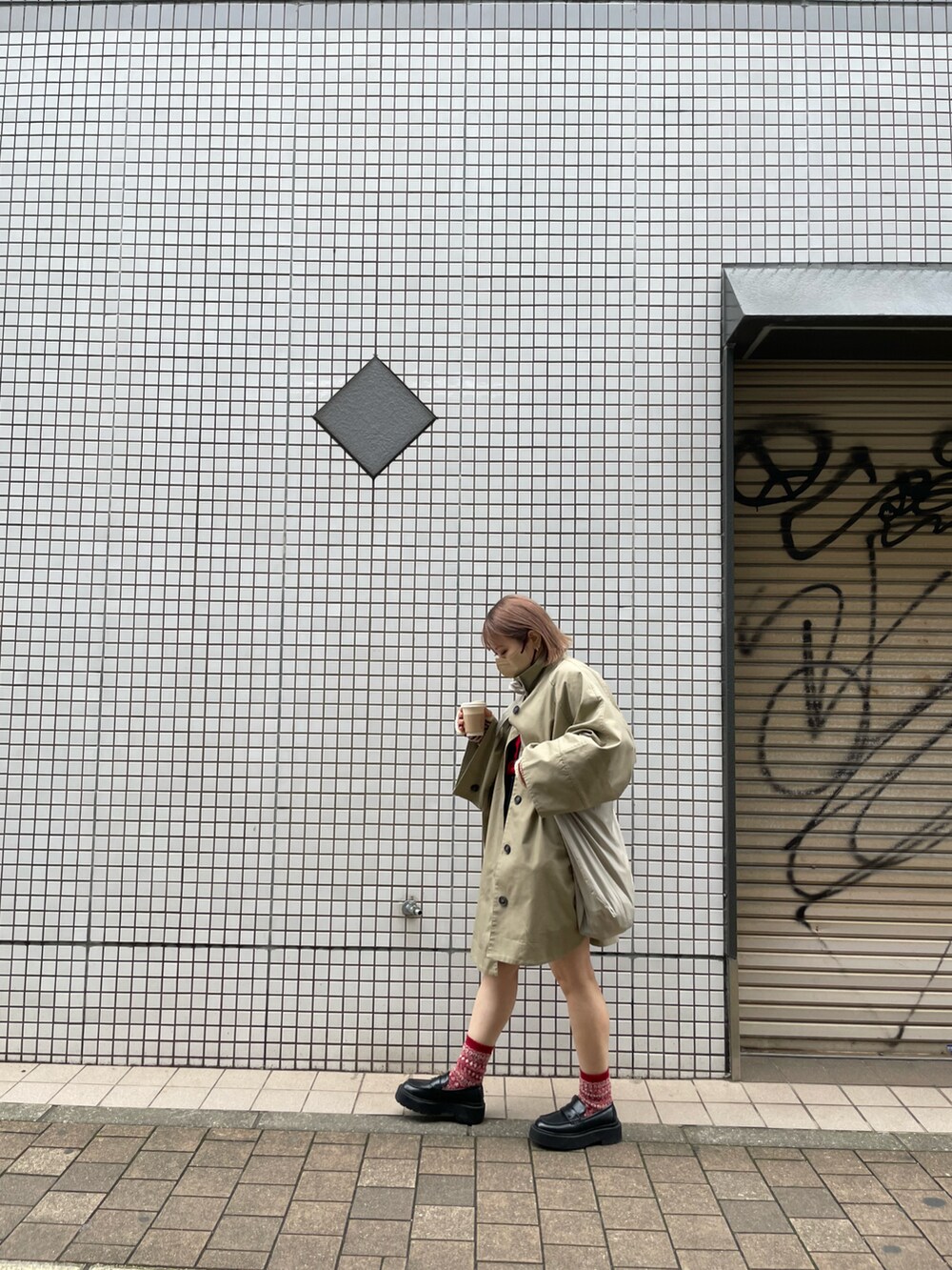 ベージュ系のポンチョ、レッド系のニット/セーター、ブラック系のパンツを着用したレディースの冬コーディネートの2枚目の写真