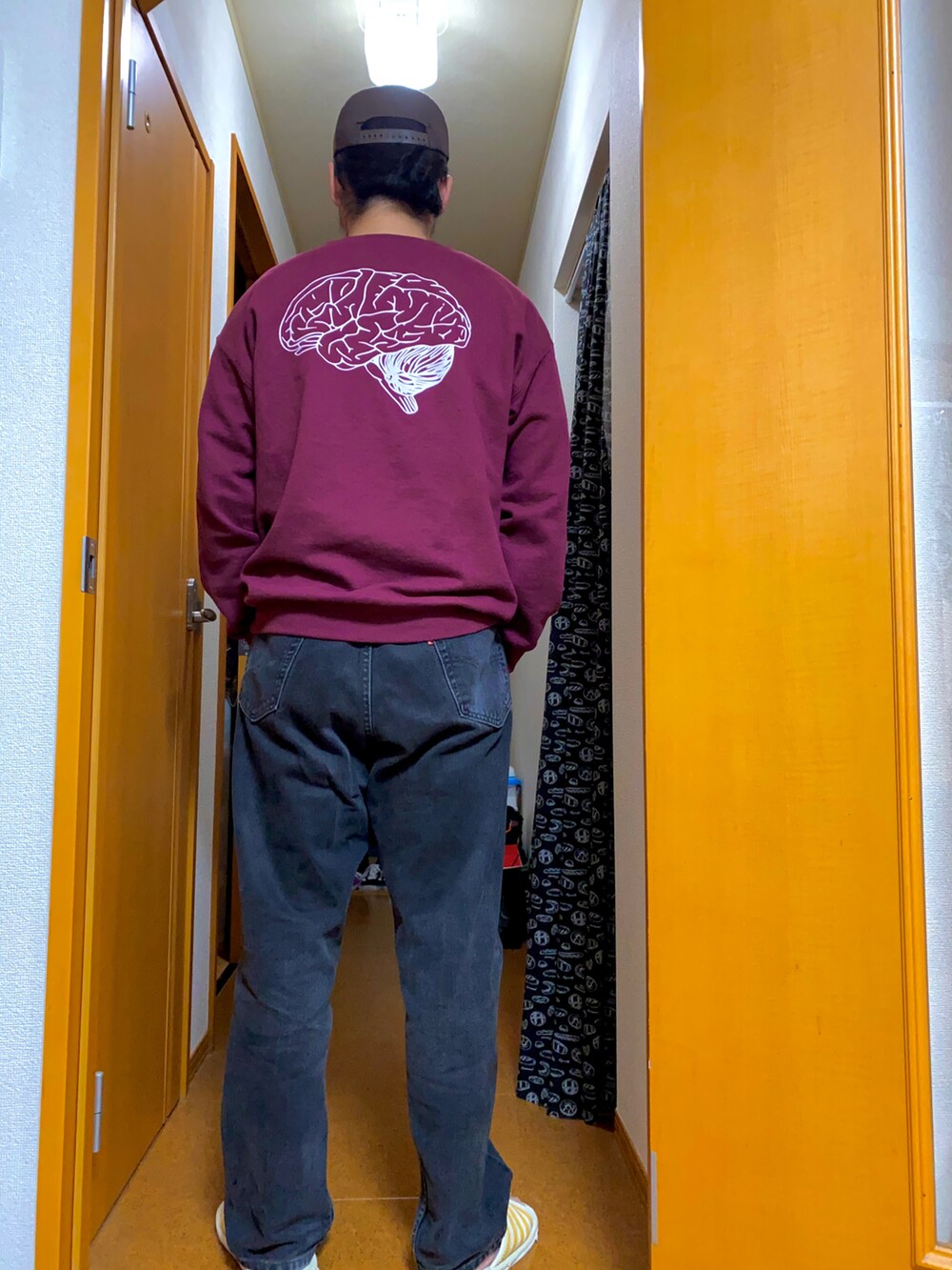 レッド系のスウェット、ブラック系のデニムパンツ、ブラウン系のキャップを着用したメンズの春コーディネートの3枚目の写真