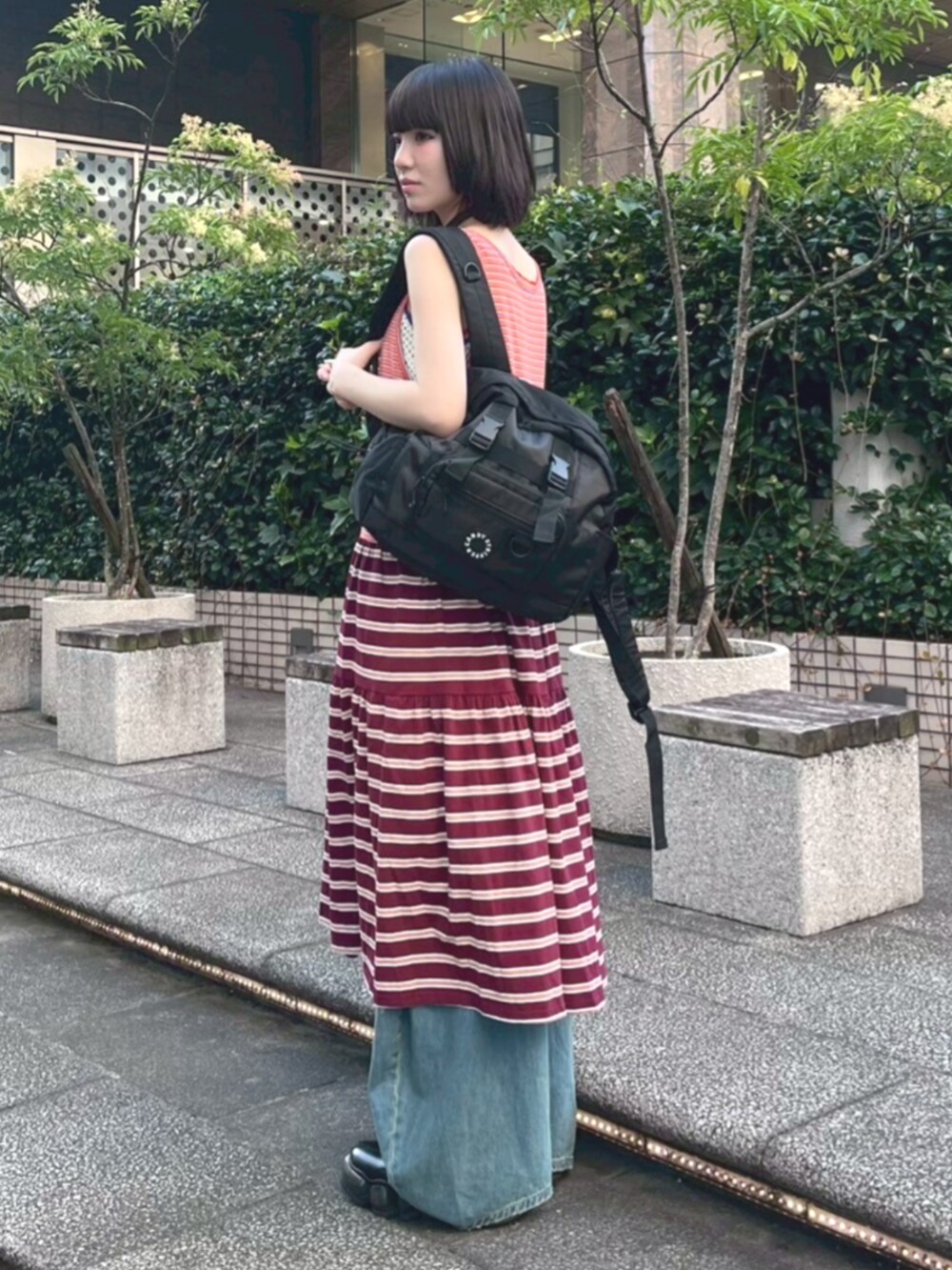 ブルー系のデニムパンツ、ブラック系のバックパック/リュック、オレンジ系のワンピースを着用したレディースの夏コーディネートの3枚目の写真