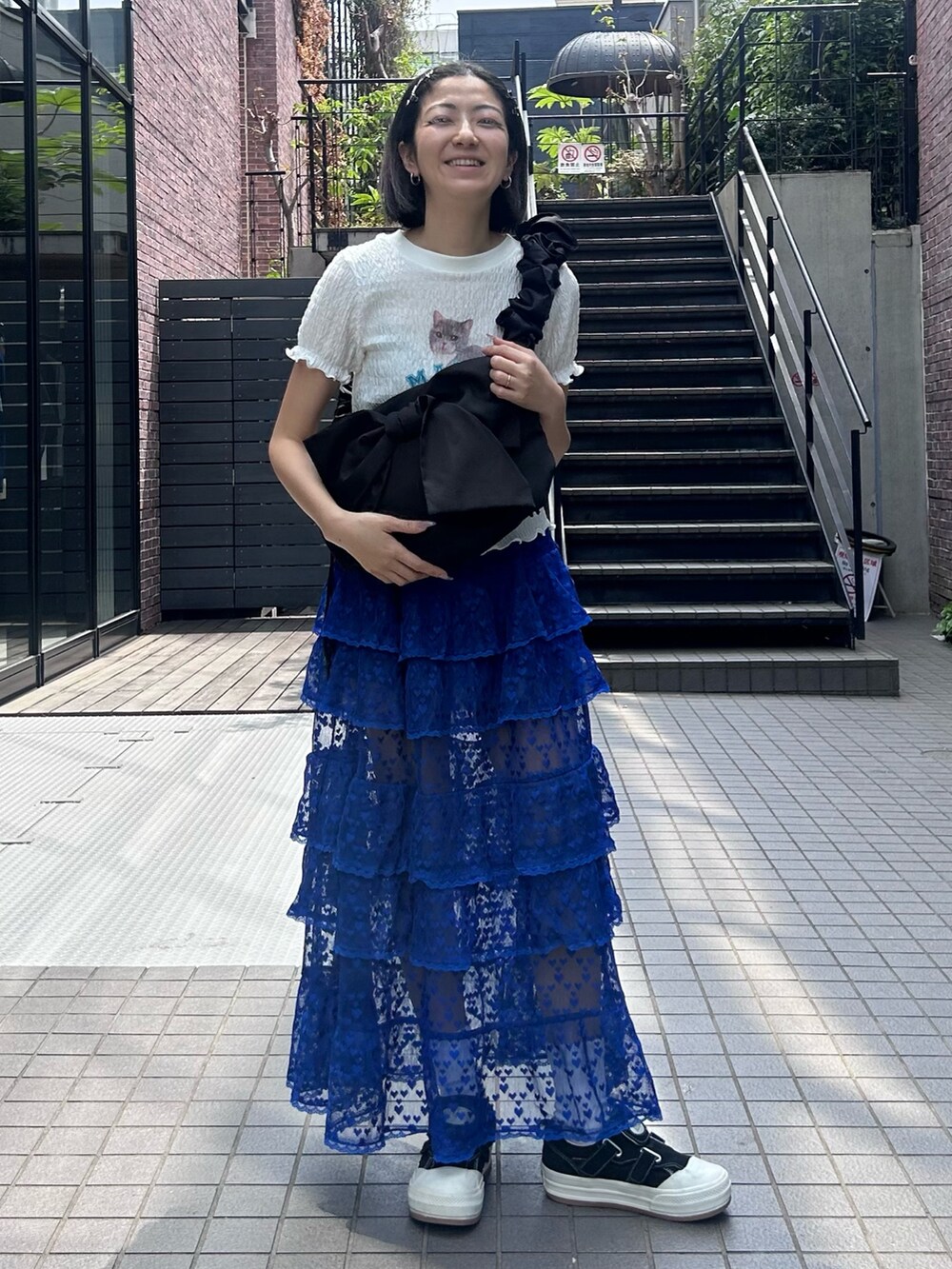 ブラック系のショルダーバッグ、ブルー系のスカート、ホワイト系のTシャツ/カットソーを着用したレディースの春コーディネートの2枚目の写真