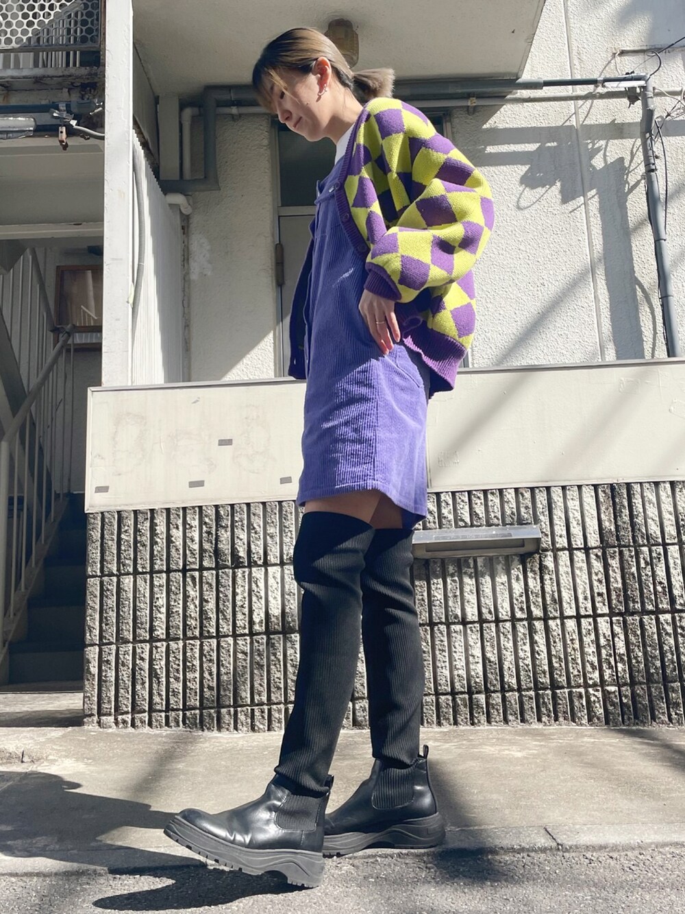 パープル系のカーディガン/ボレロ、パープル系のジャンパースカート、ブラック系のブーツを着用したレディースの春コーディネートの2枚目の写真