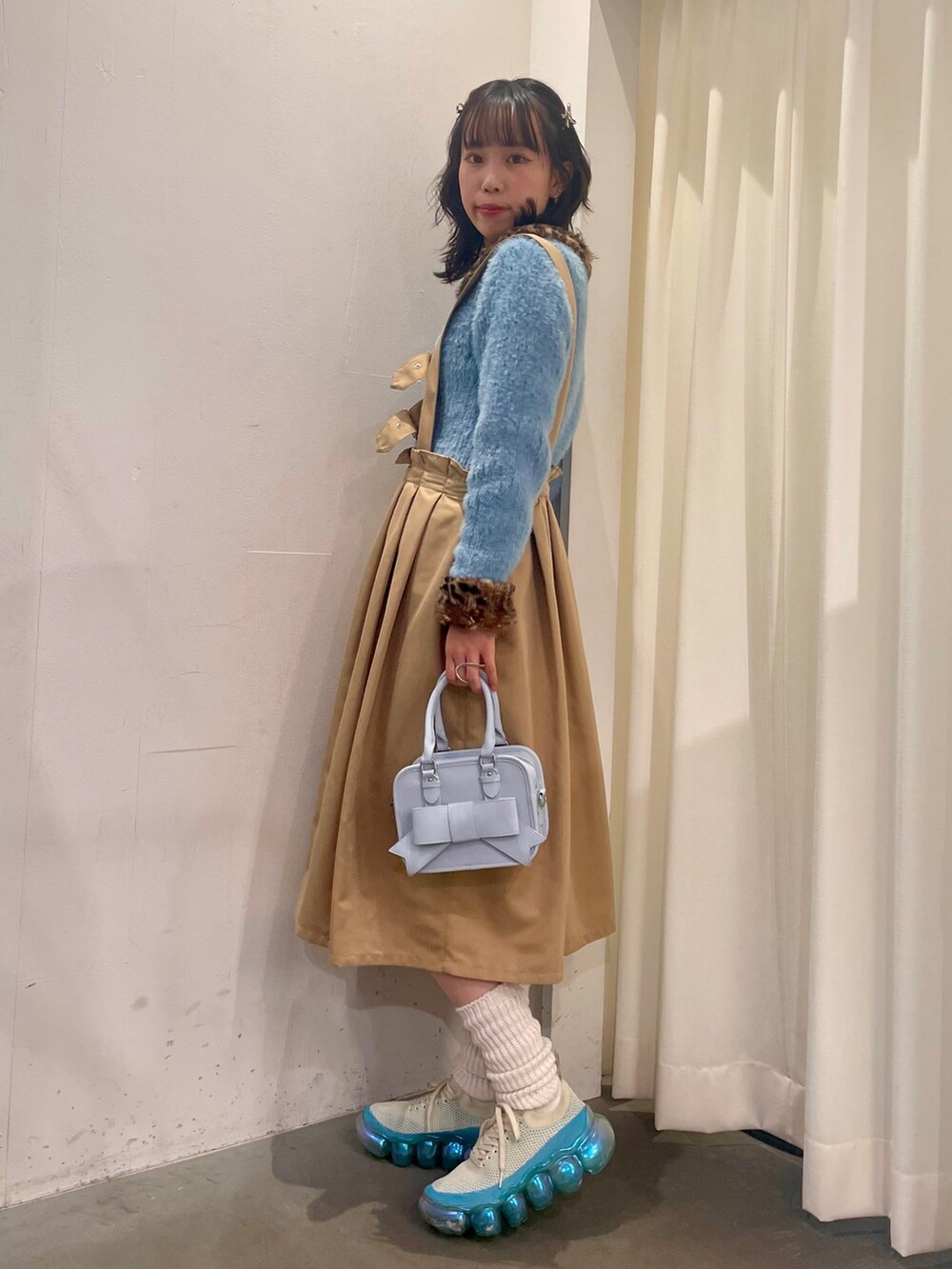 ブルー系のカーディガン/ボレロ、ベージュ系のジャンパースカート、ブルー系のショルダーバッグを着用したレディースの秋コーディネートの2枚目の写真