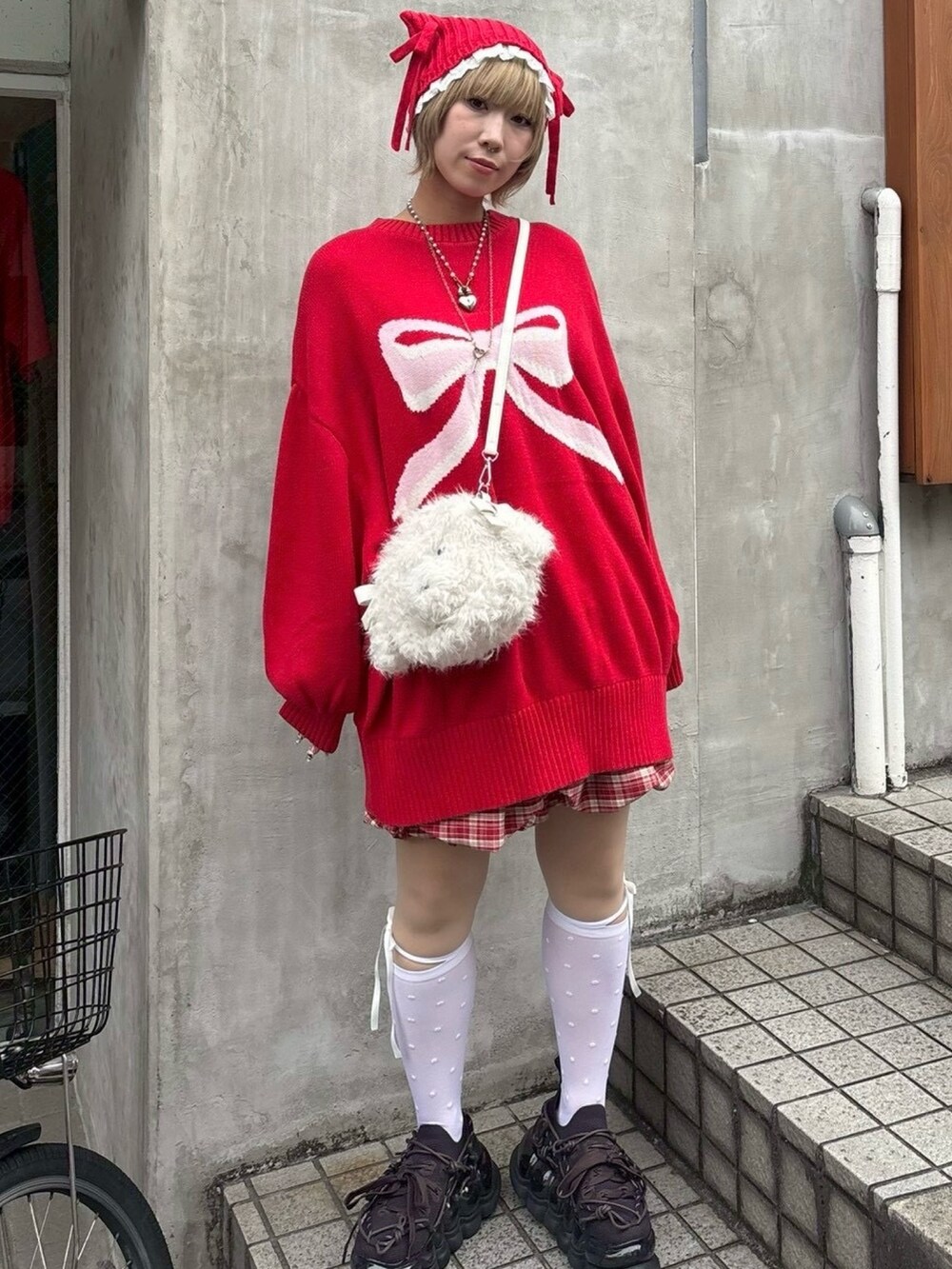 レッド系のニット/セーター、レッド系のスカート、ホワイト系のショルダーバッグを着用したレディースの秋コーディネートの2枚目の写真