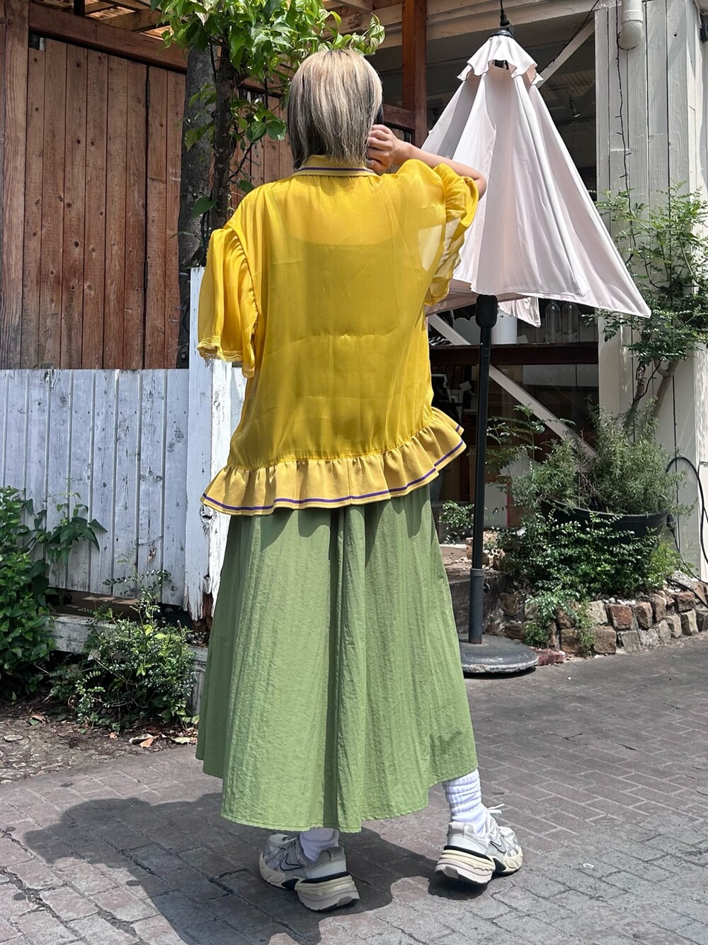 イエロー系のポロシャツ、グリーン系のジャンパースカート、シルバー系のシューズを着用したレディースの夏コーディネートの3枚目の写真