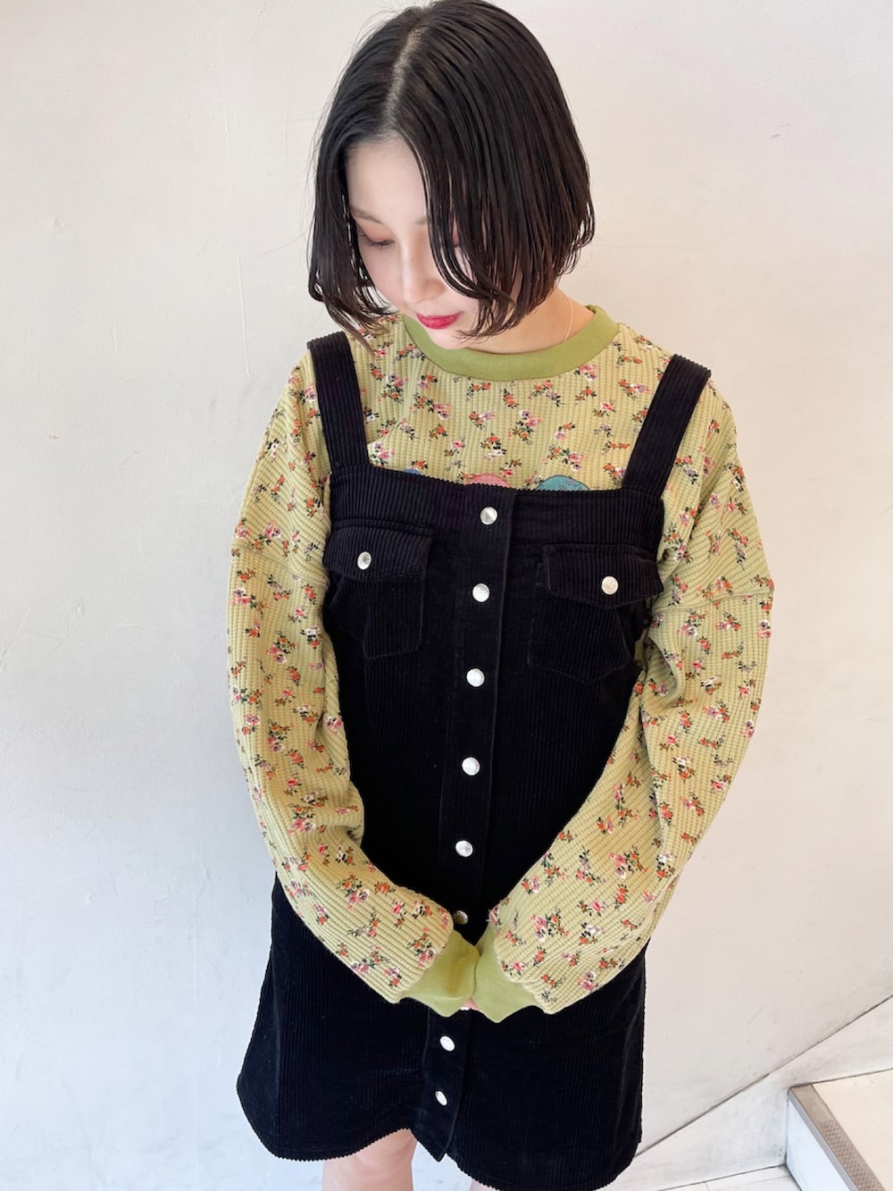 ブラック系のジャンパースカート、グリーン系のスウェット、ブラック系のスニーカーを着用したレディースの春コーディネートの2枚目の写真