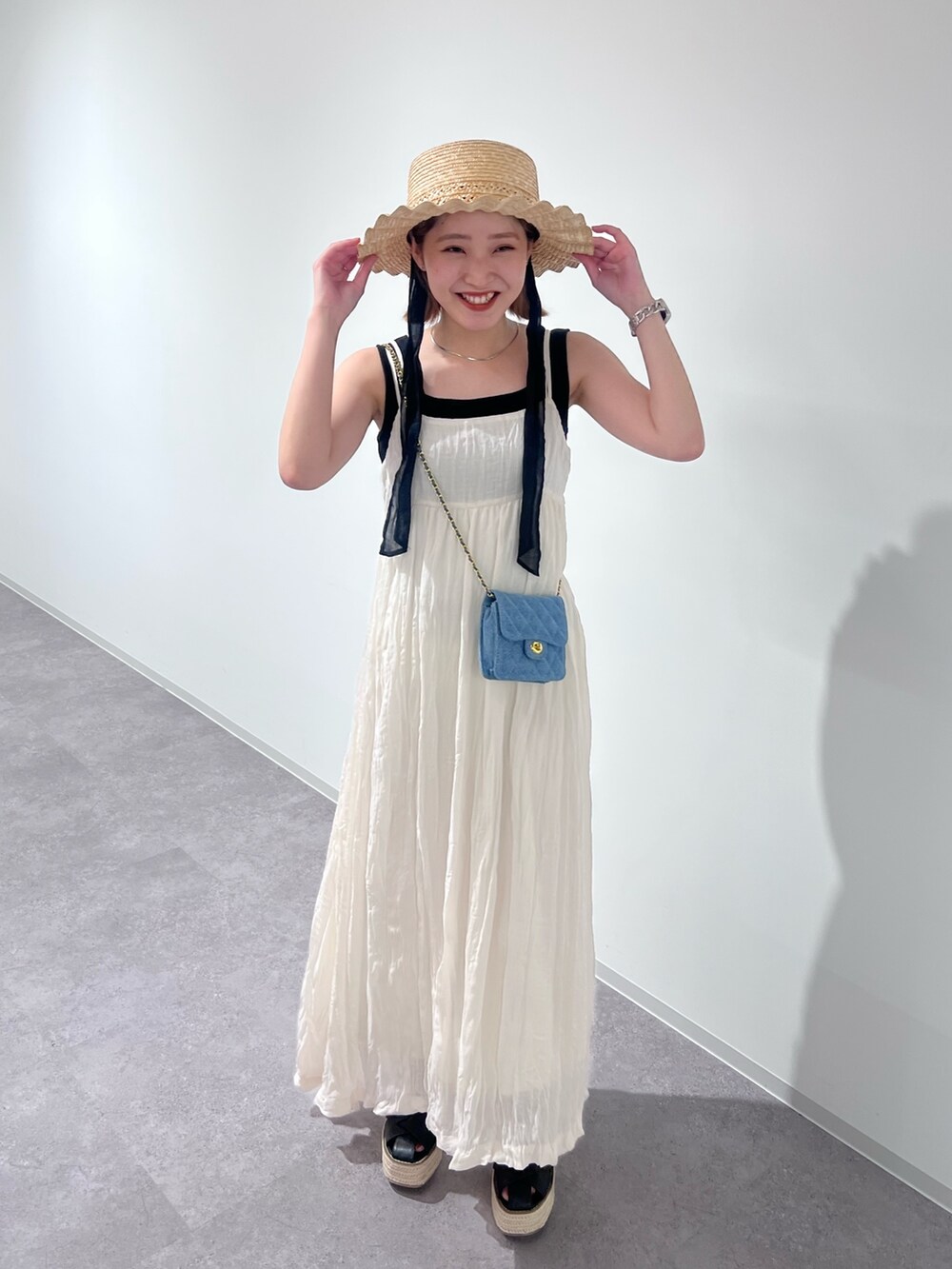 ブラック系のニット/セーター、ホワイト系のワンピース、ブルー系のショルダーバッグを着用したレディースの夏コーディネートの2枚目の写真