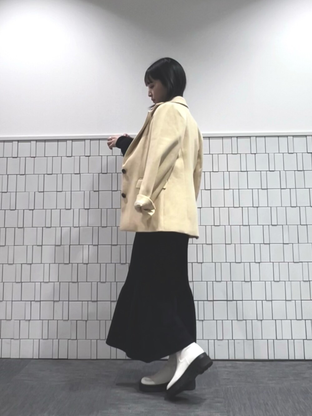 イエロー系のテーラードジャケット、ブラック系のワンピース、ホワイト系のブーツを着用したレディースの冬コーディネートの2枚目の写真