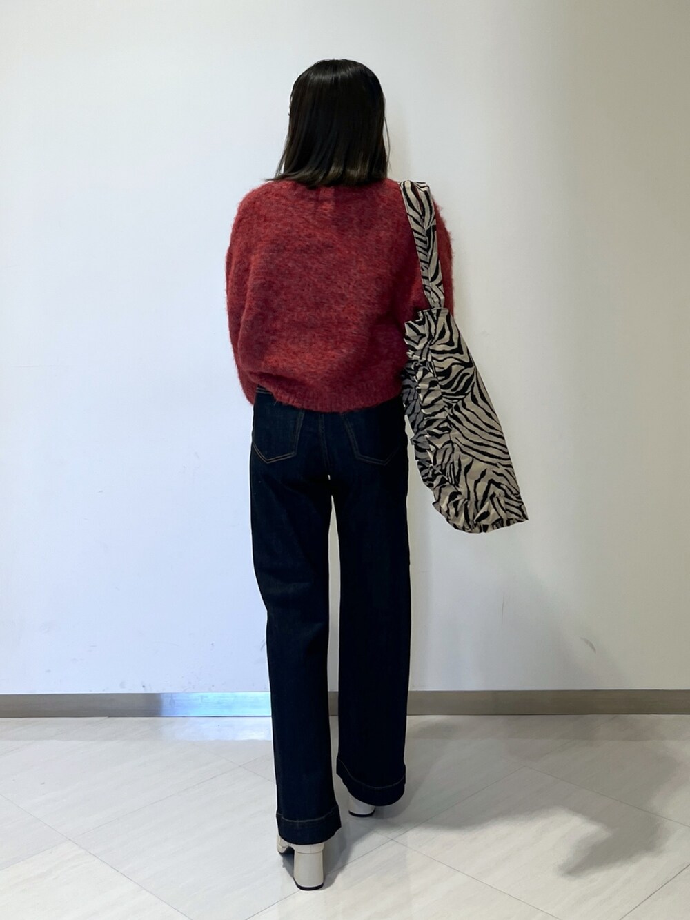 ブルー系のデニムパンツ、レッド系のニット/セーター、ベージュ系のトートバッグを着用したレディースの秋コーディネートの4枚目の写真