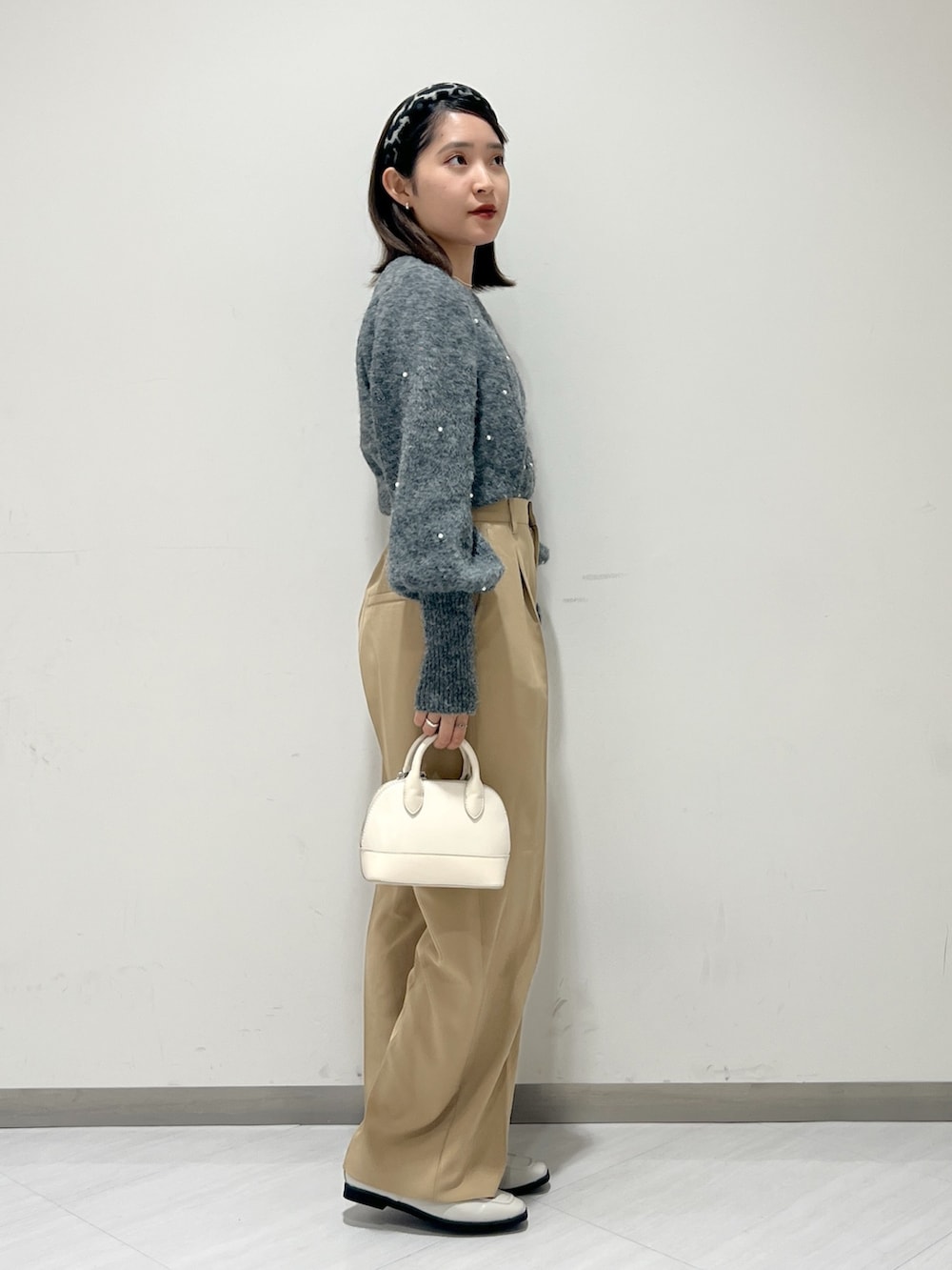 ベージュ系のスラックス、グレー系のニット/セーター、ホワイト系のショルダーバッグを着用したレディースの秋コーディネートの2枚目の写真