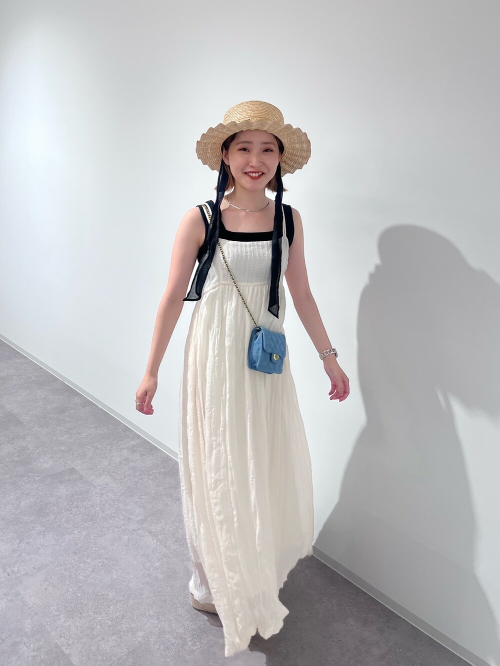 ブラック系のニット/セーター、ホワイト系のワンピース、ブルー系のショルダーバッグを着用したレディースの夏コーディネートの3枚目の写真