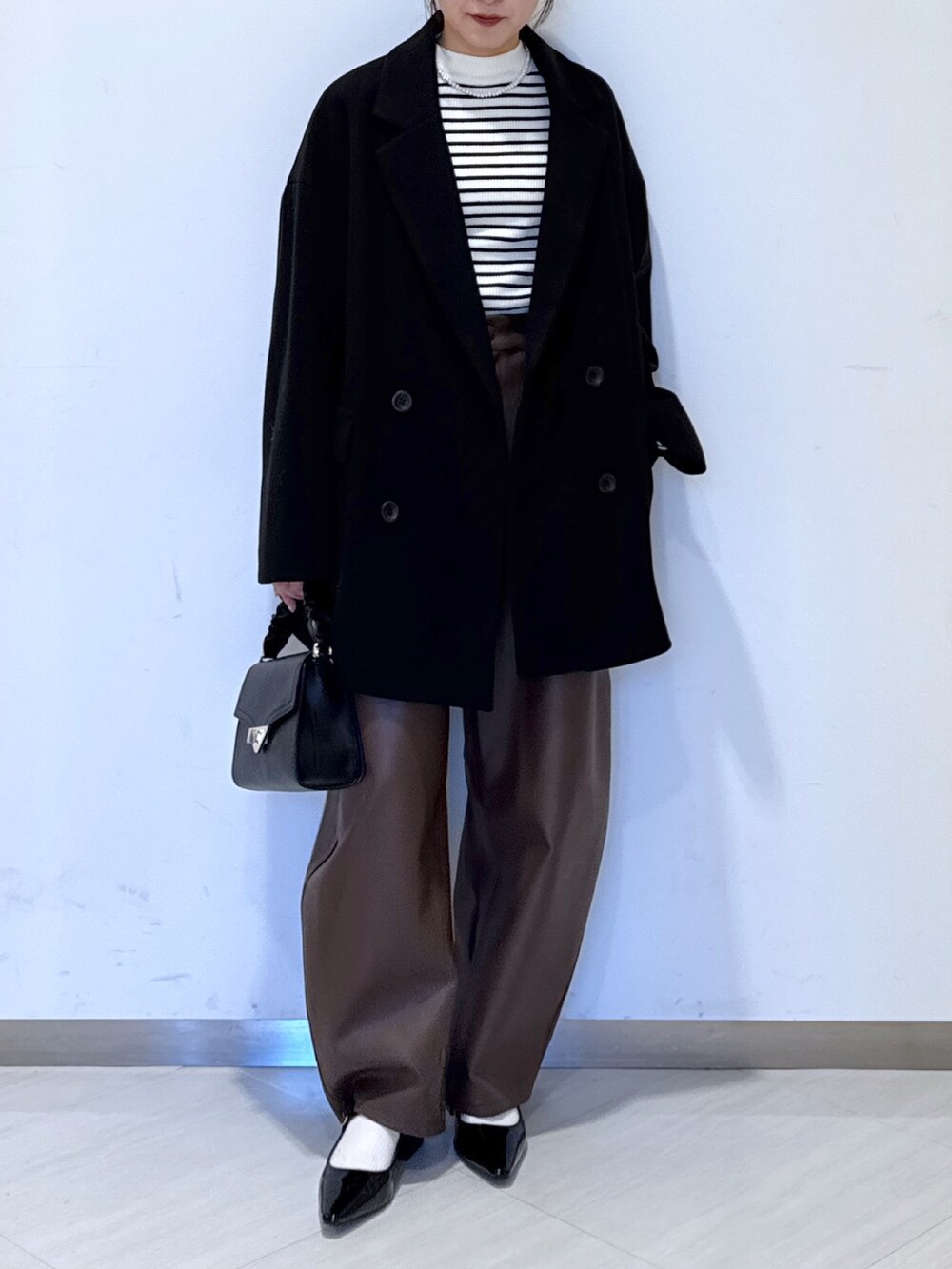 ブラック系のパンプス、ブラック系のショルダーバッグ、ホワイト系のニット/セーターを着用したレディースの秋コーディネートの2枚目の写真