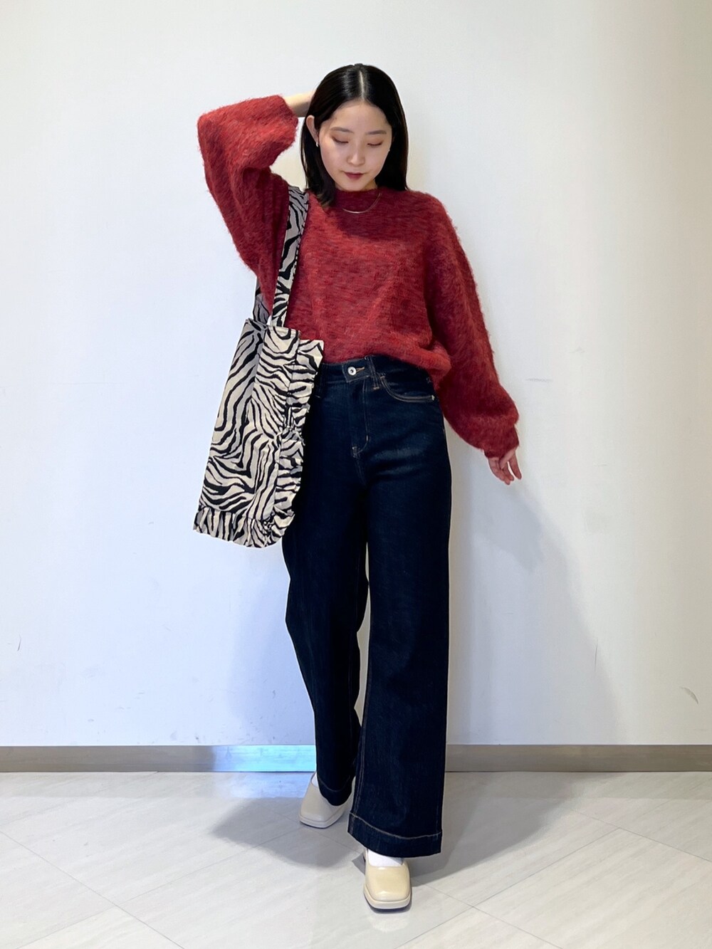 ブルー系のデニムパンツ、レッド系のニット/セーター、ベージュ系のトートバッグを着用したレディースの秋コーディネートの2枚目の写真