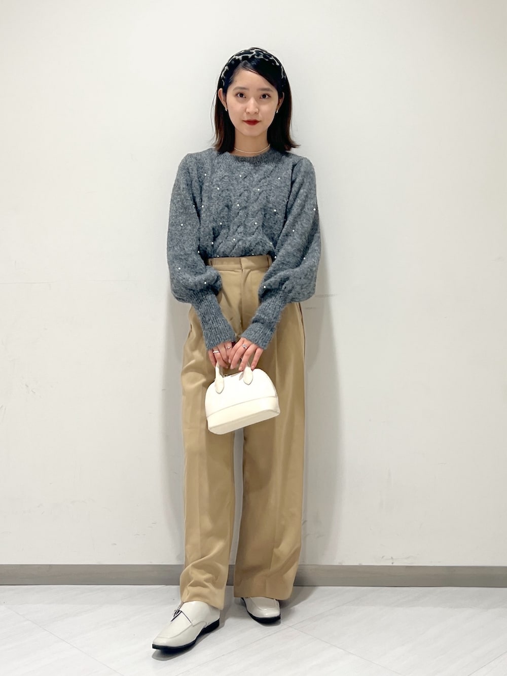 ベージュ系のスラックス、グレー系のニット/セーター、ホワイト系のショルダーバッグを着用したレディースの秋コーディネートの3枚目の写真