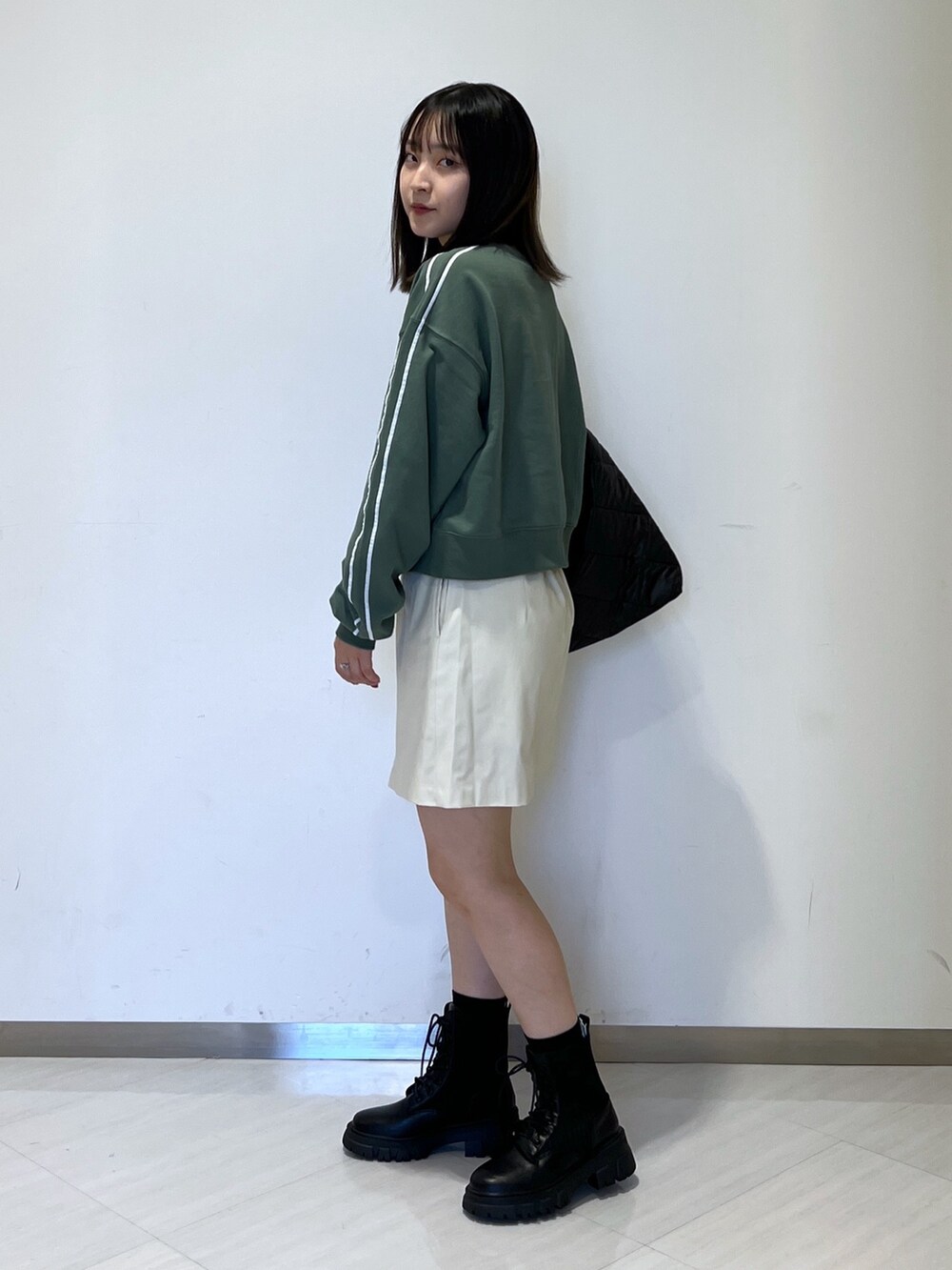 グリーン系のスウェット、ホワイト系のスカート、ブラック系のトートバッグを着用したレディースの秋コーディネートの4枚目の写真