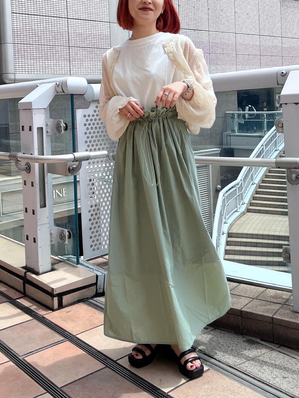 グリーン系のワンピース、ホワイト系のシャツ/ブラウス、ブラック系のサンダルを着用したレディースの春コーディネートの2枚目の写真