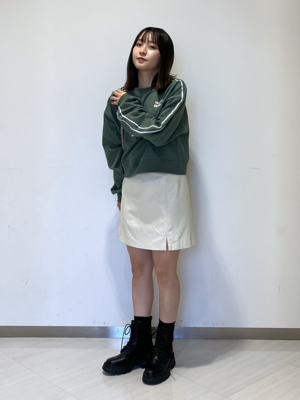 グリーン系のスウェット、ホワイト系のスカート、ブラック系のトートバッグを着用したレディースの秋コーディネートの2枚目の写真