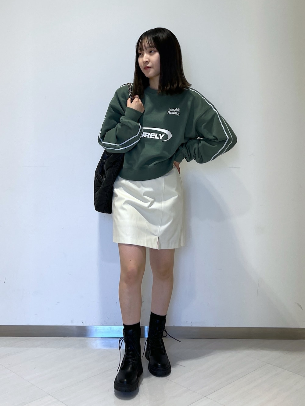 グリーン系のスウェット、ホワイト系のスカート、ブラック系のトートバッグを着用したレディースの秋コーディネートの3枚目の写真