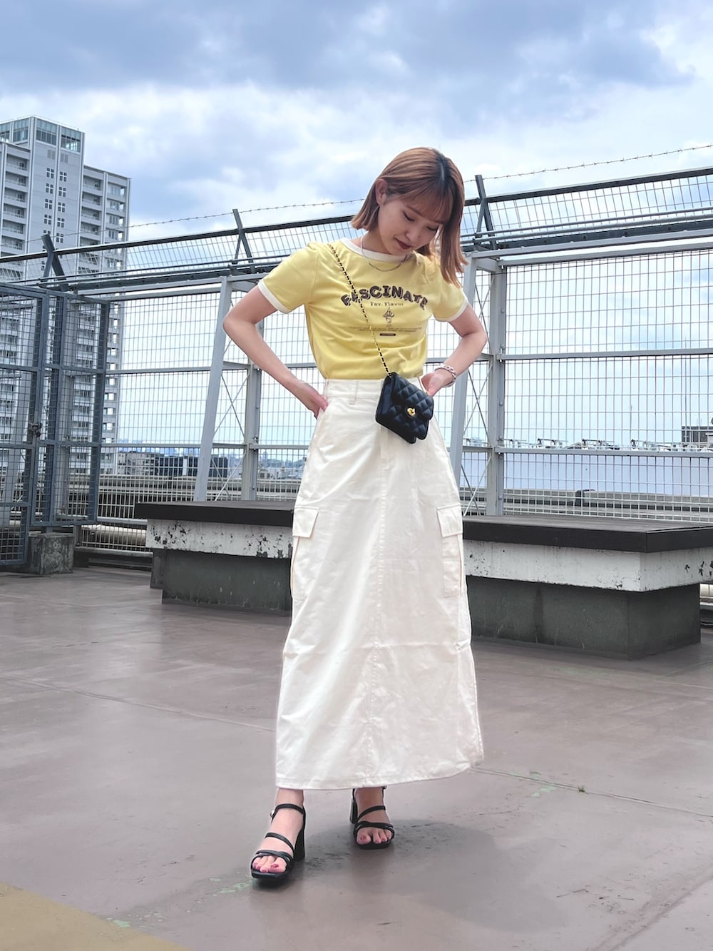 ホワイト系のスカート、イエロー系のTシャツ/カットソー、ブラック系のショルダーバッグを着用したレディースの夏コーディネートの2枚目の写真