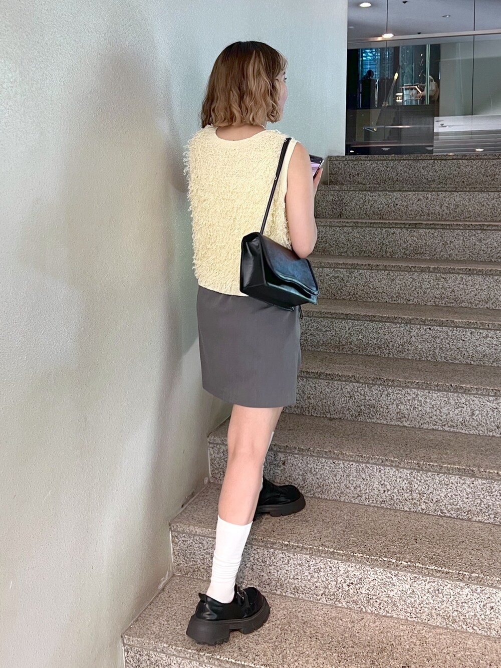 グレー系のスカート、イエロー系のニット/セーター、ホワイト系のキャミソールを着用したレディースの夏コーディネートの4枚目の写真